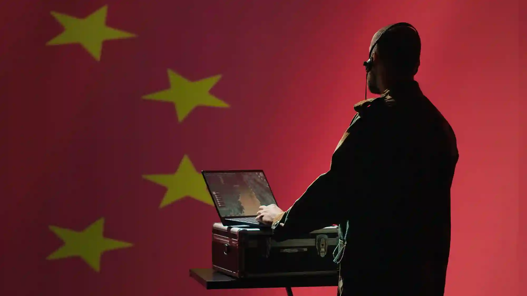 A silhouetted operator working on a laptop against a Chinese flag background, representing foreign state-sponsored cyber intelligence operations.