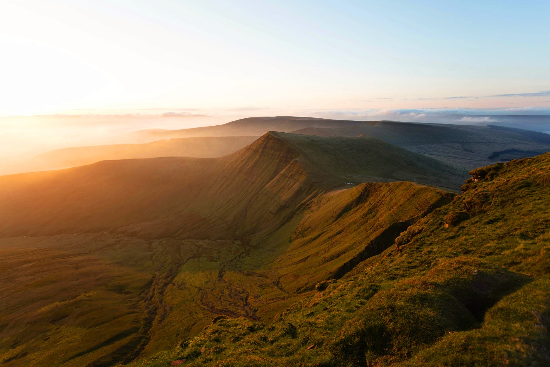 Sunrise over Pen y Fan in the Brecon Beacons, with golden light casting shadows across the green mountains and valleys.