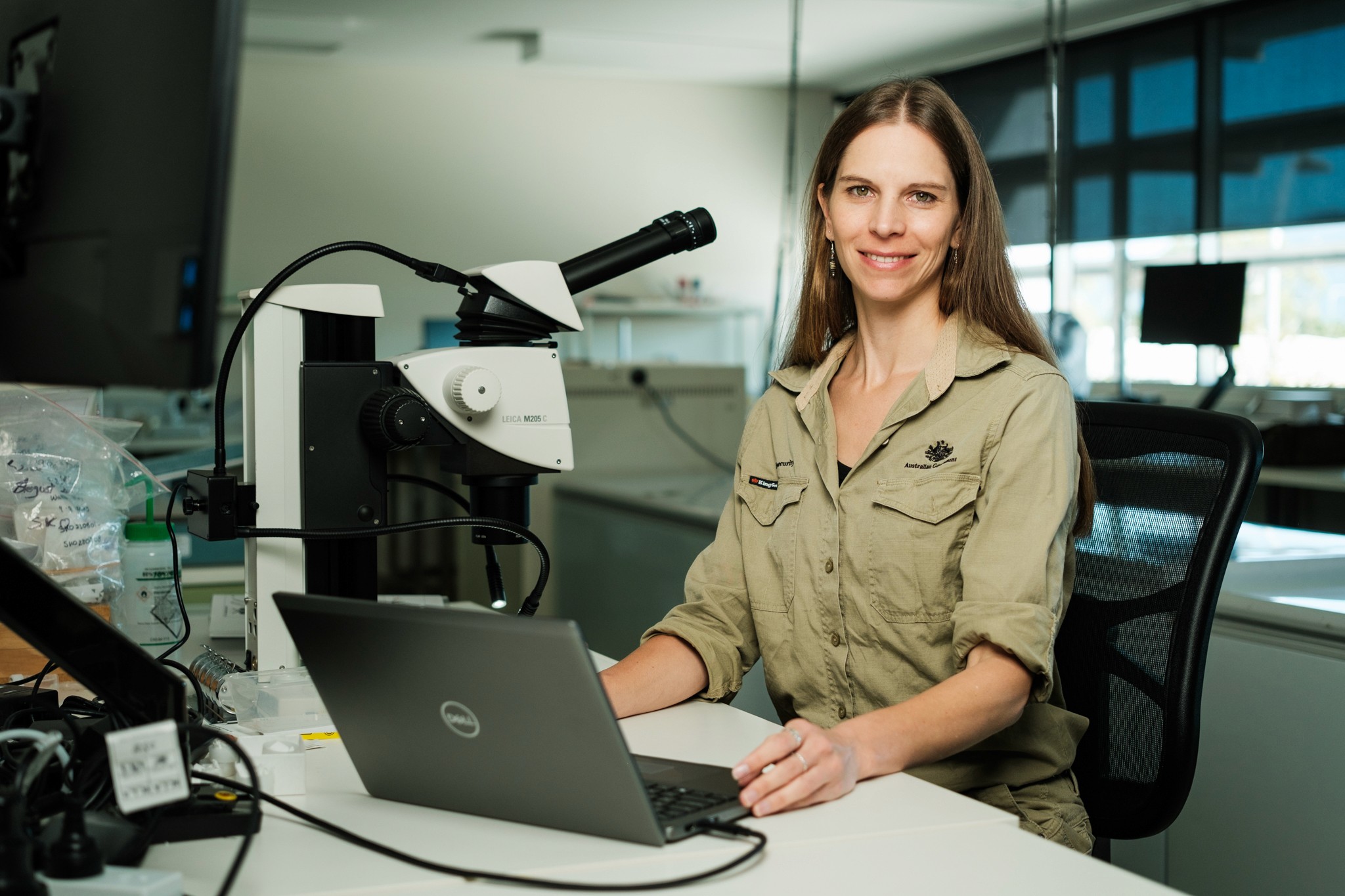 A woman sits in a lab next to a microscope