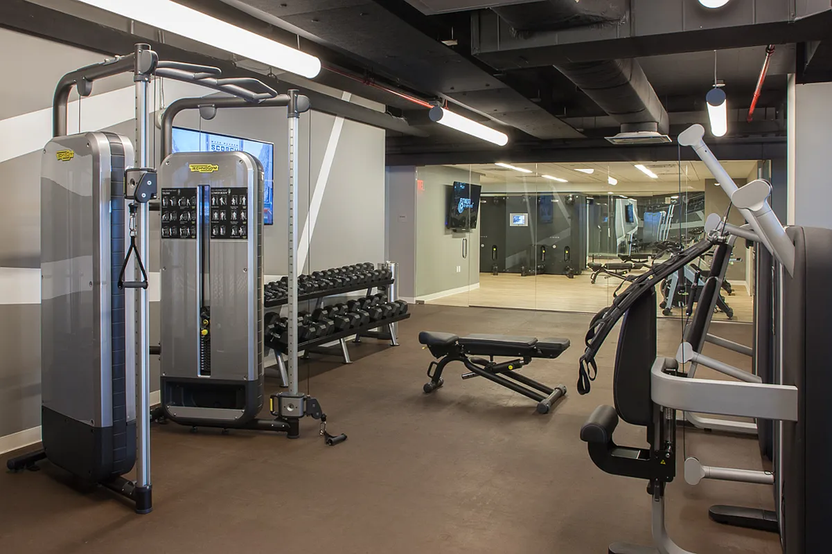 A gym room featuring various exercise equipment and large mirrors reflecting the workout space.