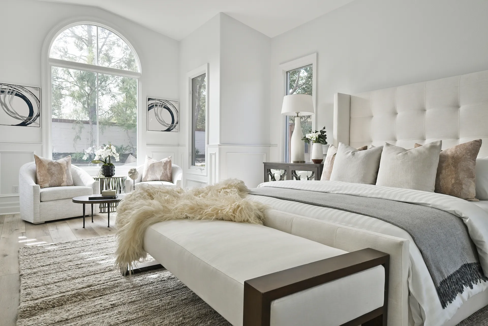 View of the master bedroom suite, revealing beautiful decor, a comfortable bed, and a seating area, all bathed in natural sunlight from the arched windows. Photo by Todd Huge.