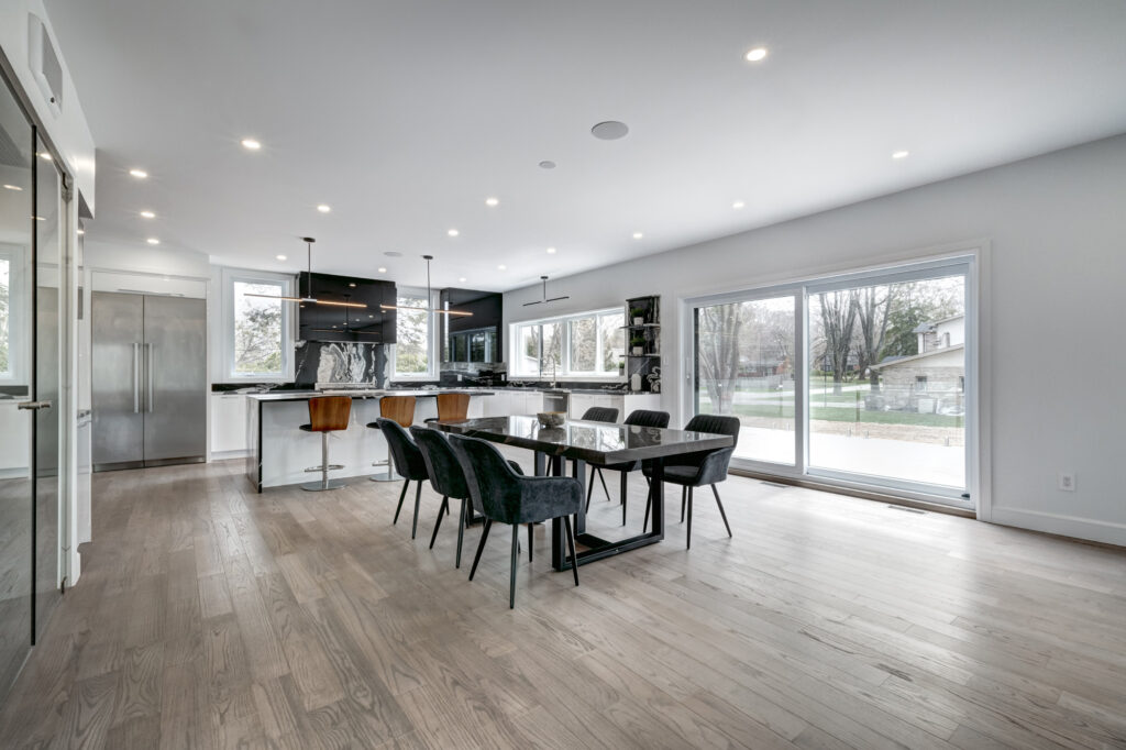 Bright open-concept kitchen and dining area with black and white marble waterfall island, sleek white cabinetry, and glass staircase, showcasing B&Y Reno Corp’s custom kitchen remodeling in a modern luxury home.