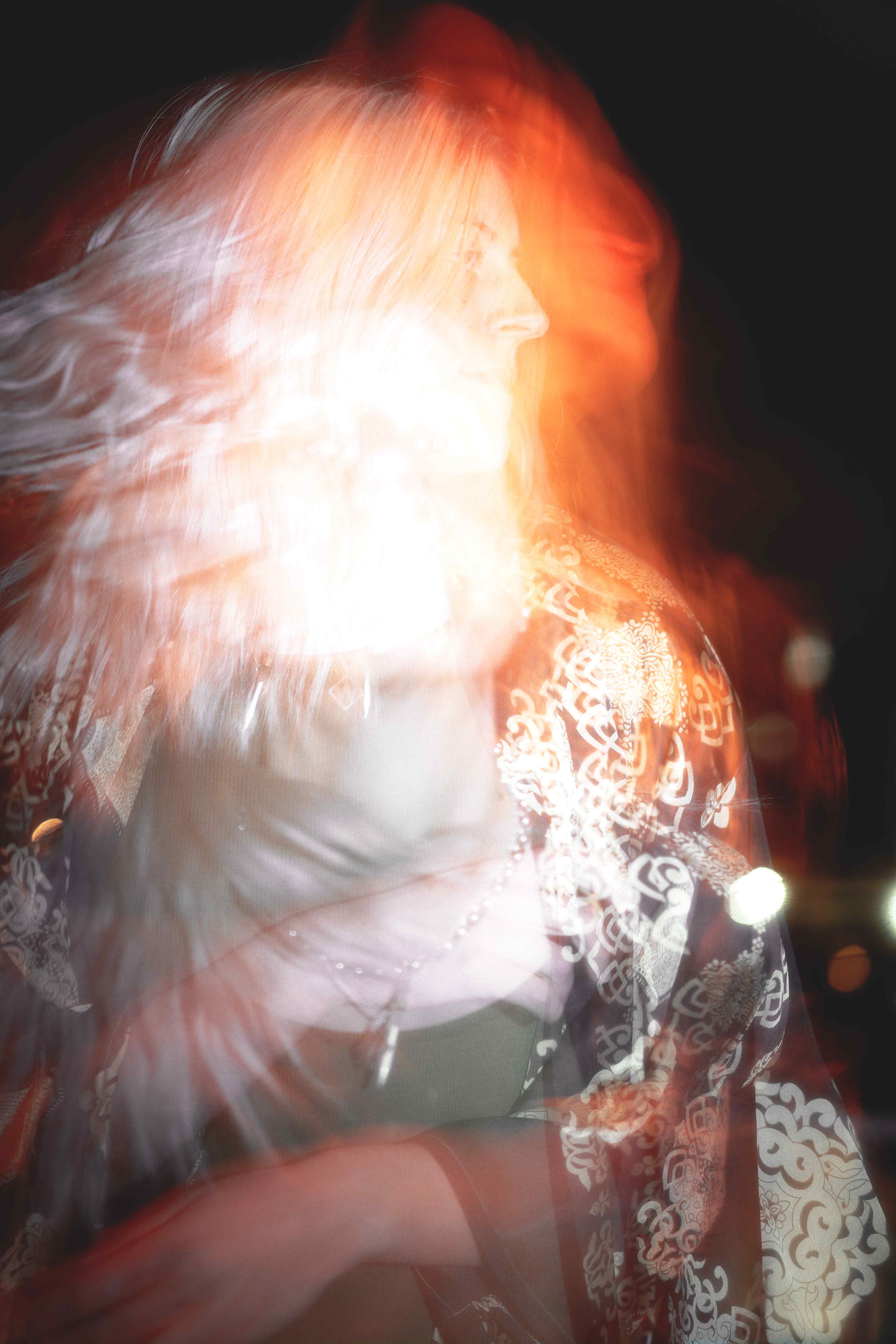 Photographie de portrait créative avec plusieurs déclenchements de flash laissant paraître un effet de filé couplé à plusieurs immobilisations d'une femme bougeant avec élégance dans une lueur rouge