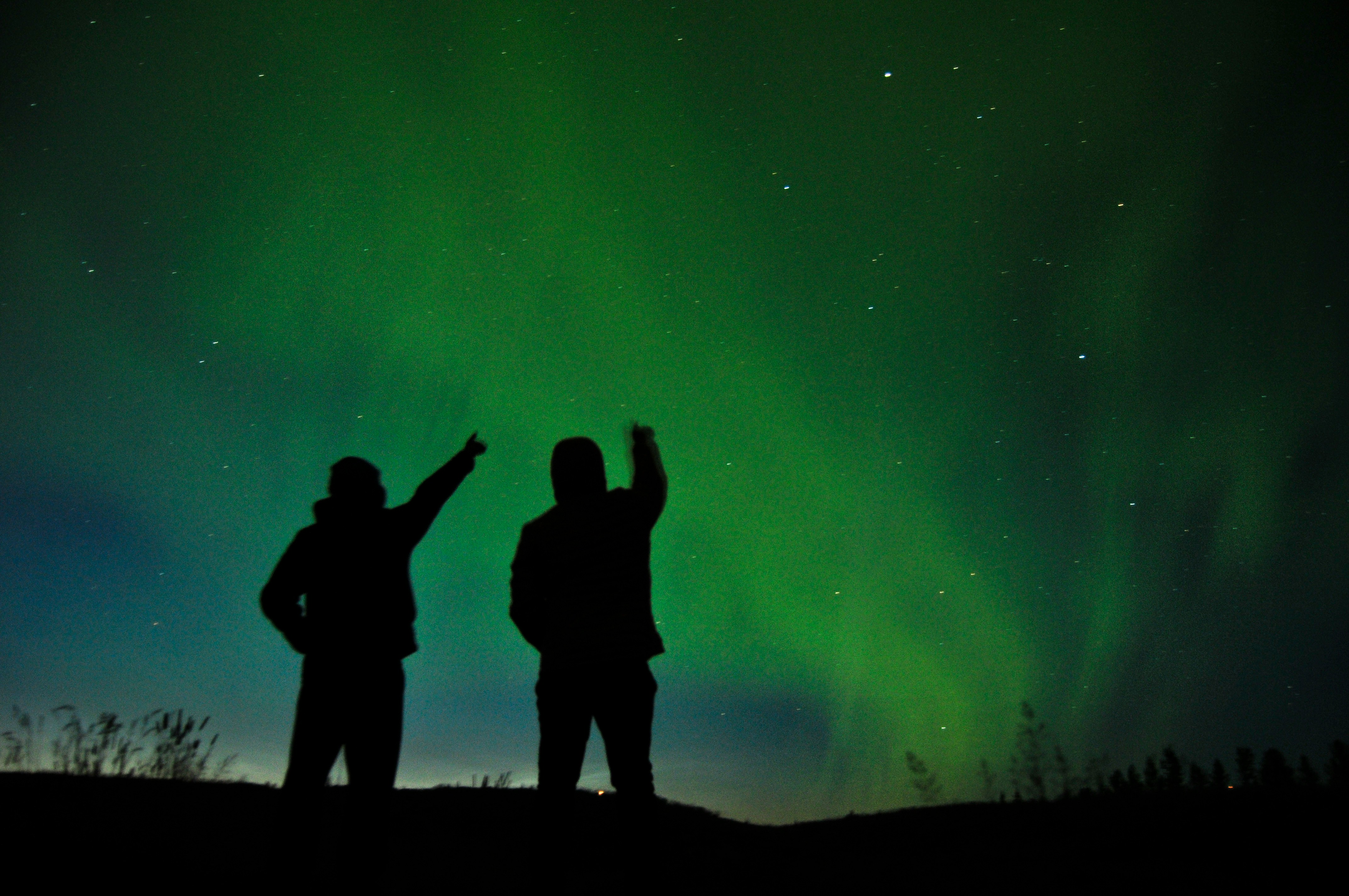 Two people watching and pointing at the Northern Lights in Iceland.