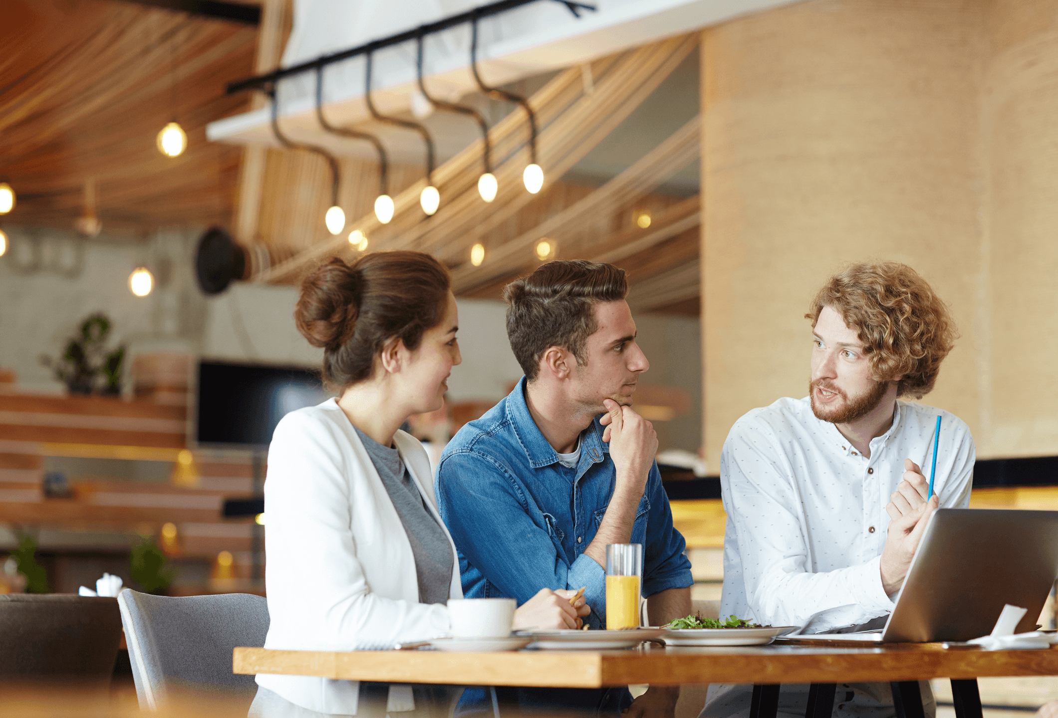 Three coworkers talking around a laptop in a café.