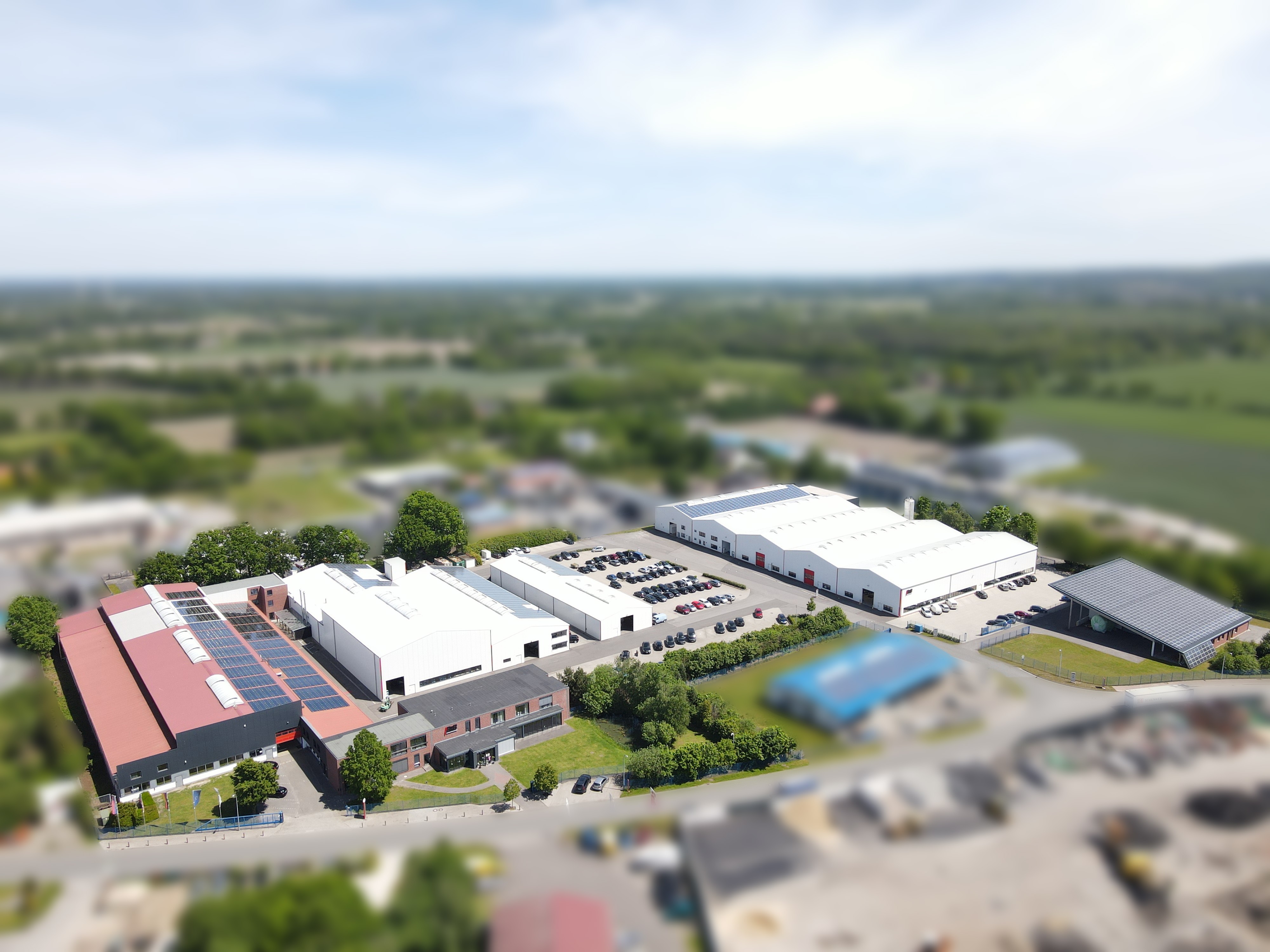 Industrieanlage im Freien mit Fabrikgebäuden, Parkplätzen und Grünflächen.  Luftaufnahme einer Produktionsstätte.