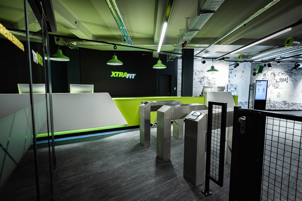 Eingangsbereich des XTRAFIT Fitnessstudios in Sindelfingen mit moderner Theke, eine großen LED-Bildschirm und Drehkreuz.