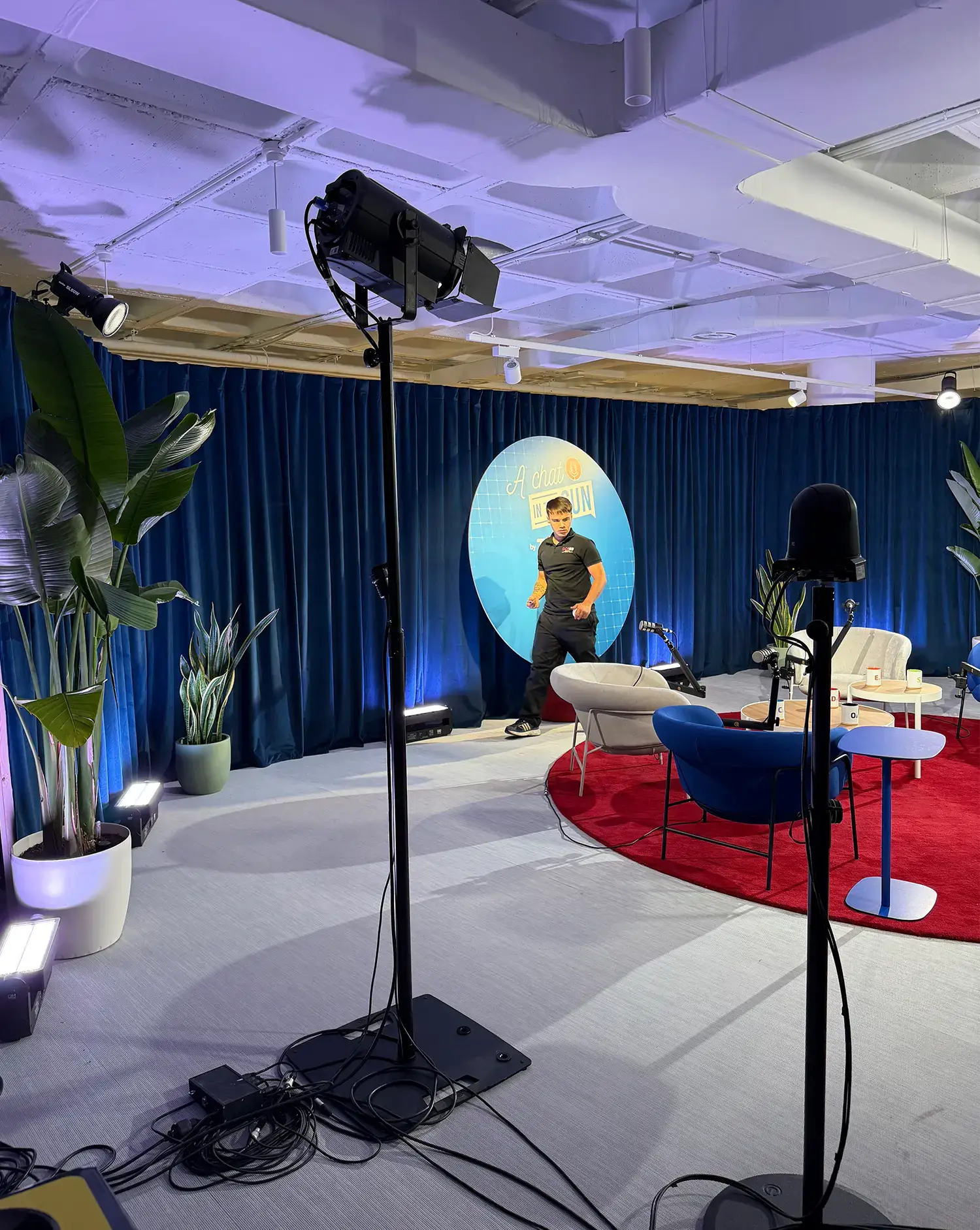 Estudio de grabación moderno con decorado azul y rojo, plantas y equipo de iluminación.