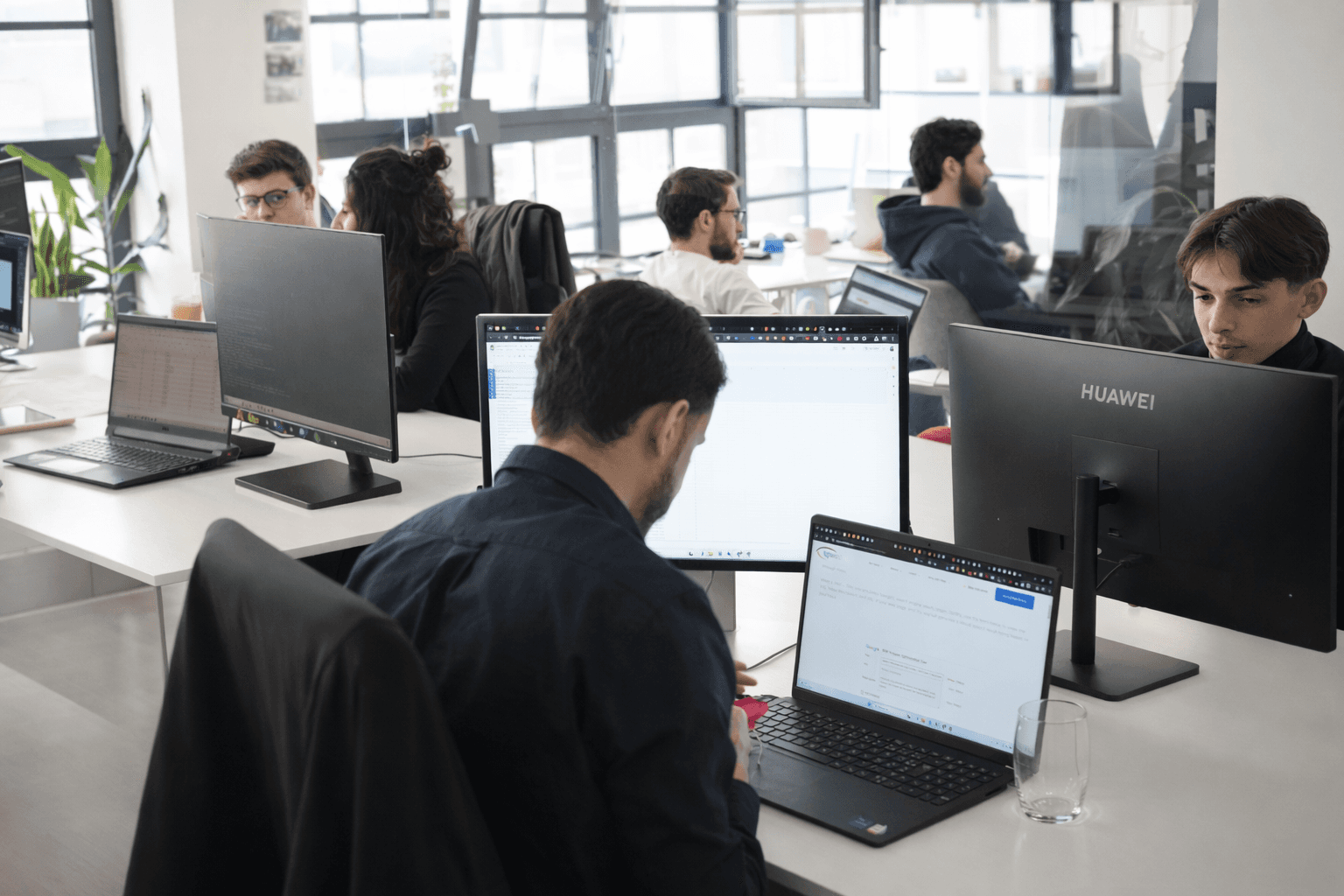 Modern red brick apartment or office building viewed from below against a blue sky, showcasing its geometric architecture with evenly spaced windows and balconies.