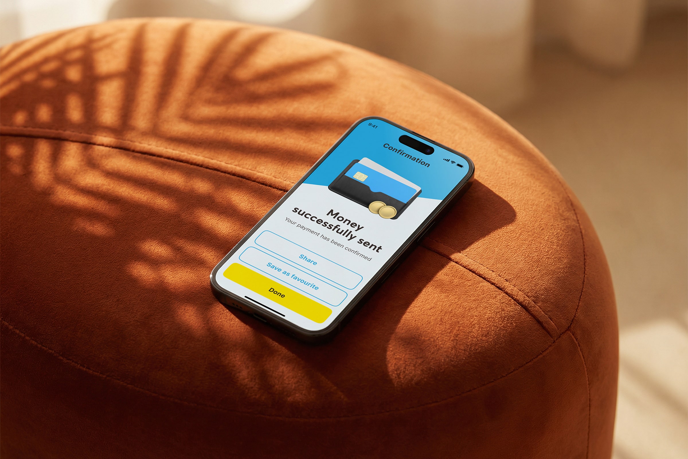 NCBA mobile app payment confirmation screen resting on an orange velvet ottoman, showing "Money successfully sent" with share and done actions.