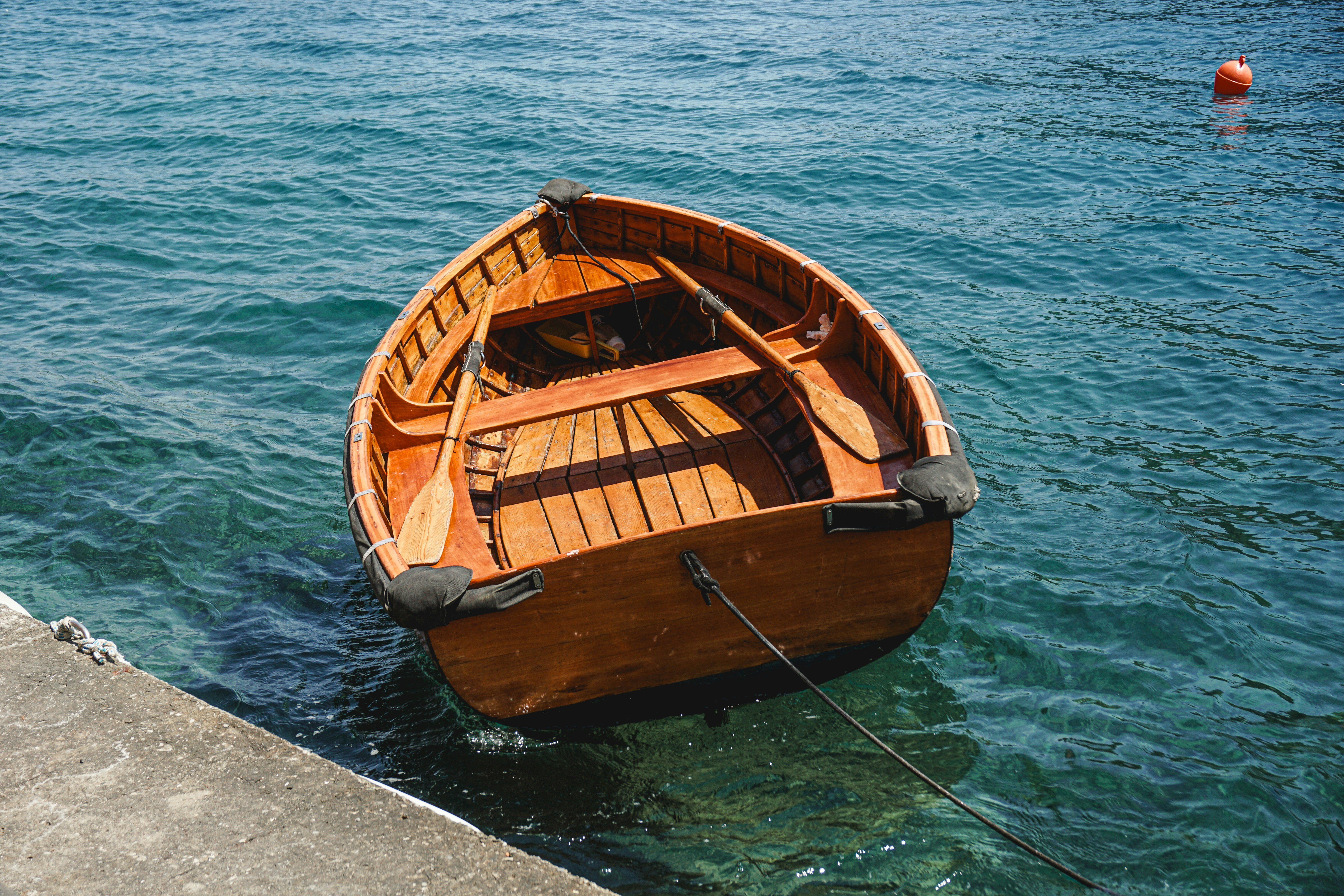 A wooden rowboat floats on clear blue water.
