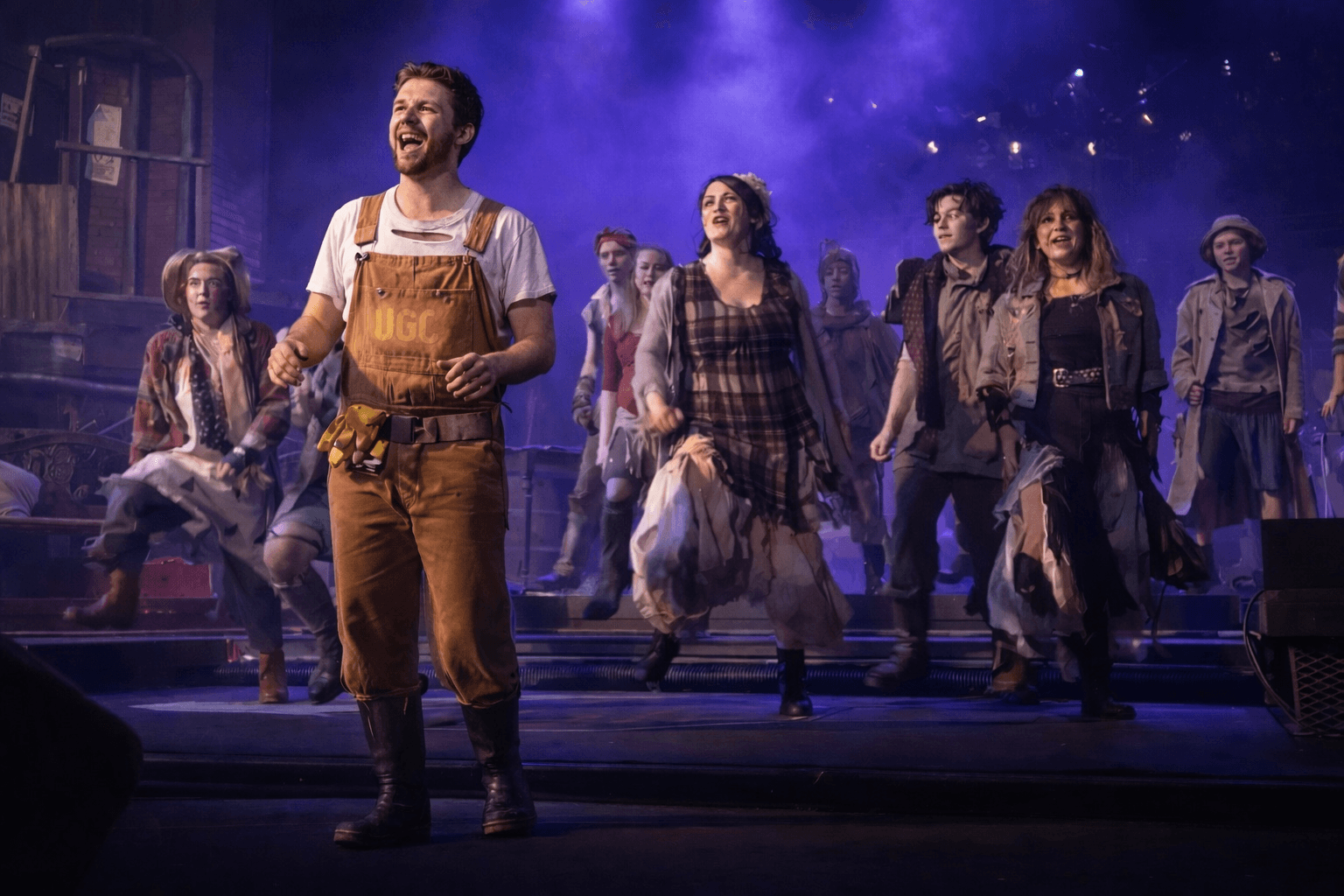Group of performers on stage under dramatic spotlights in a theatrical production setting, viewed from the audience."