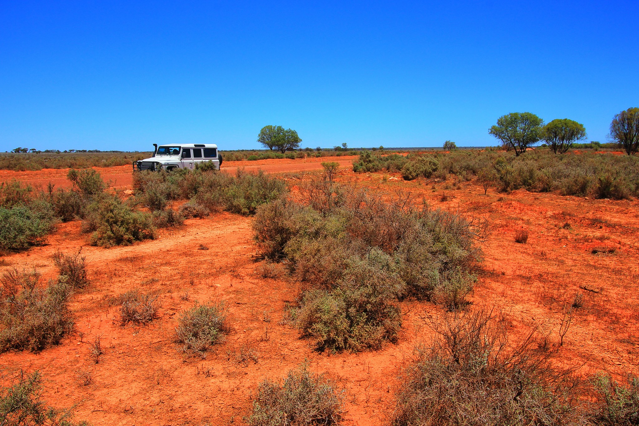 Scientist wearing safety goggles and blue lab attire, using a pipette to transfer liquid into a vial in a laboratory setting.