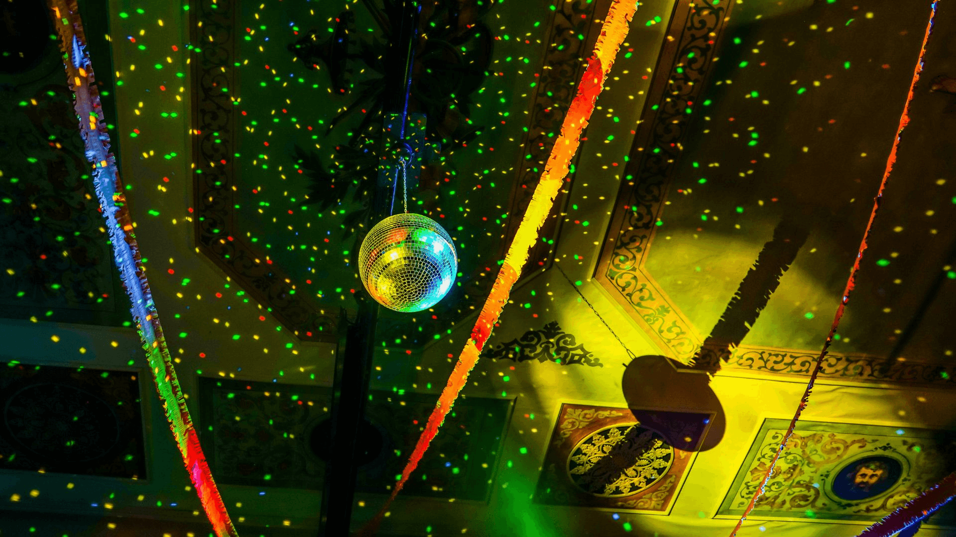 Disco ball casting coloured lights across an ornate ceiling decorated with paper streamers