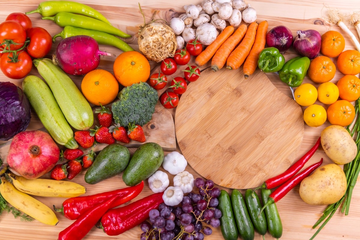 Fresh fruits and vegetables arranged around a wooden cutting board, examples of naturally gluten-free whole foods