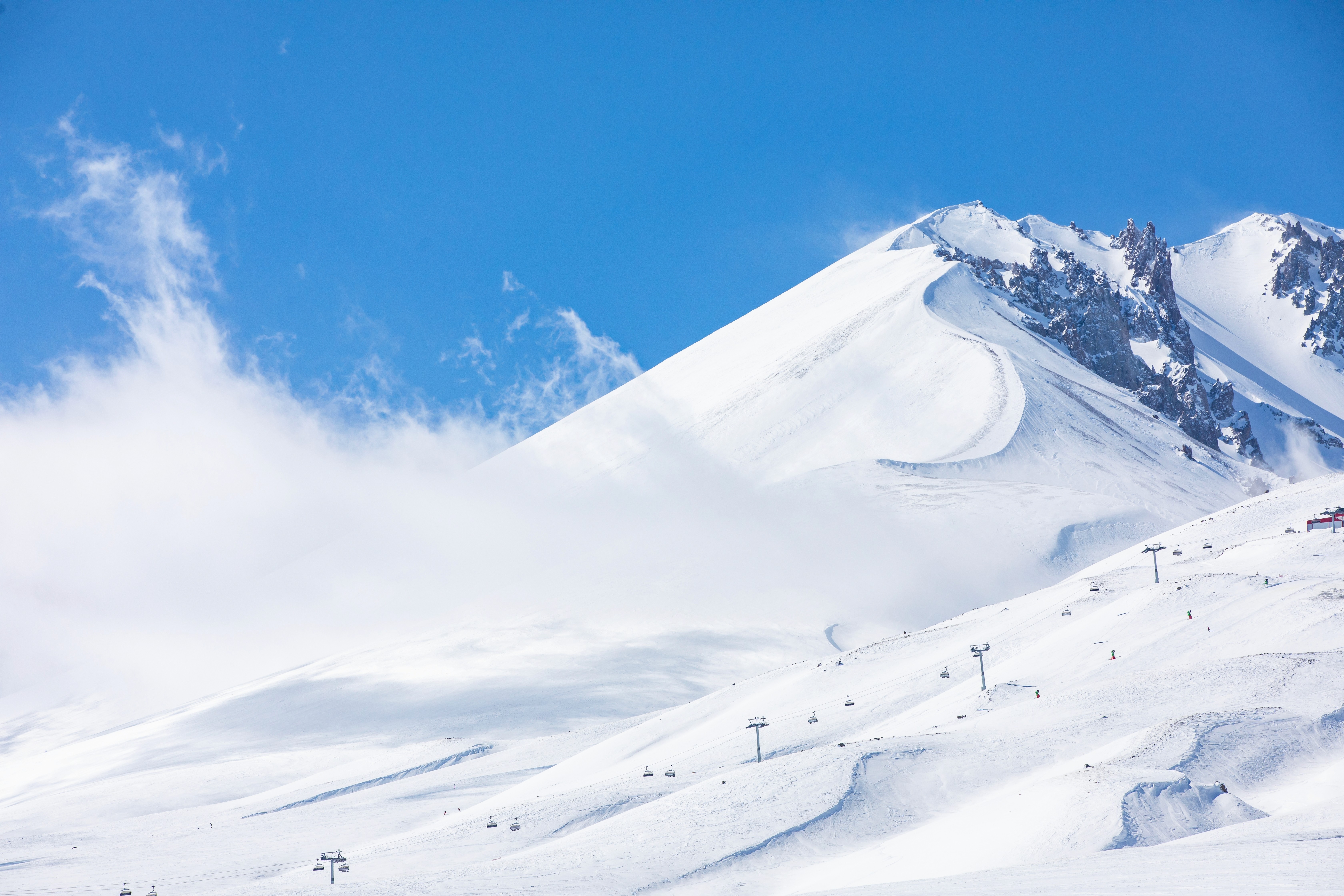 A bright, snow-covered volcanic peak with chairlifts scattered across wide open slopes under a clear blue sky.