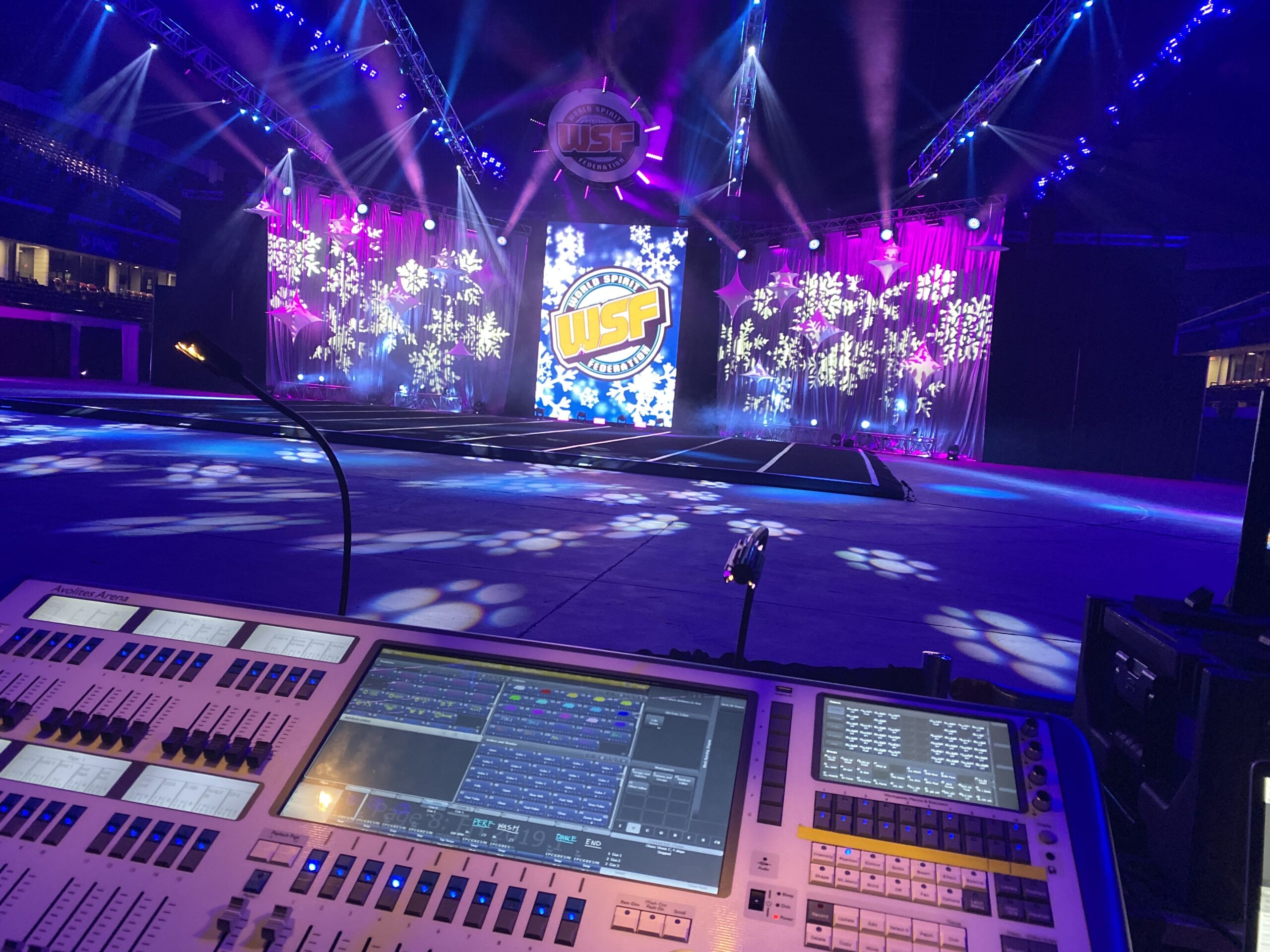 Lighting control console at front of house with an illuminated concert stage behind