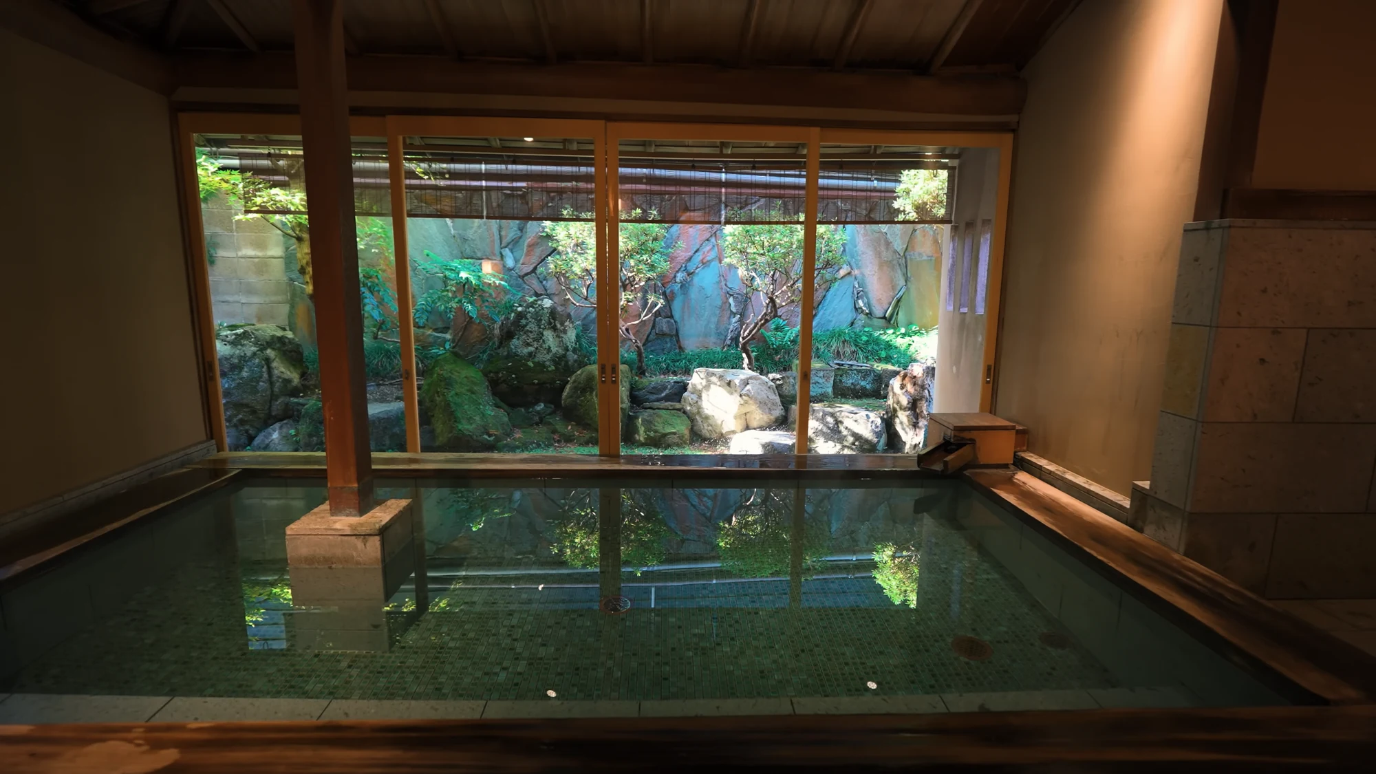 A public bath in Kinosaki with a stone pool and a planted garden visible through full-height glazing.