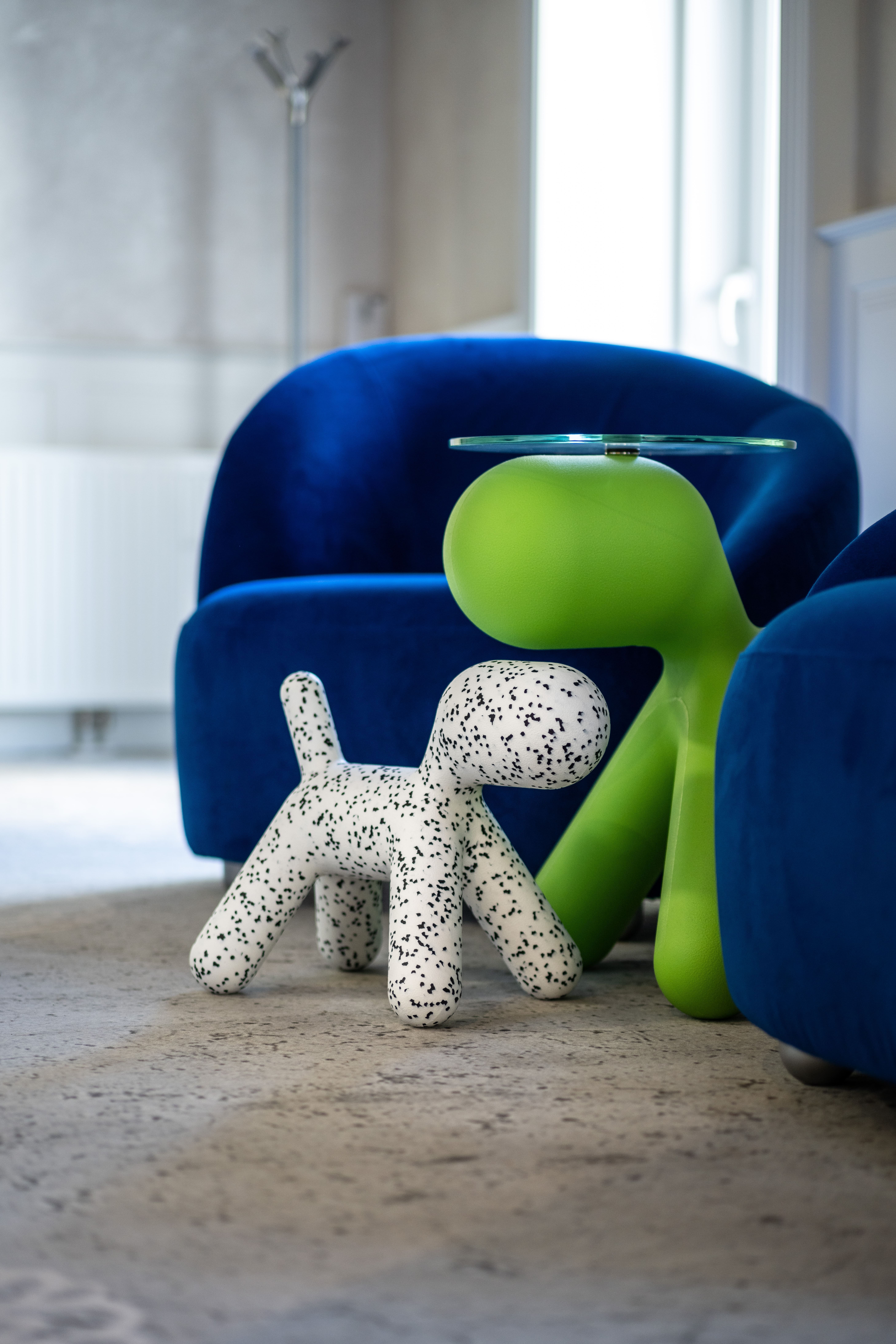 Verspieltes Inneneinrichtungs-Detail: blauer Samtsessel, grüner Beistelltisch und Magis Puppy Dekofigur im MW Interior Showroom – modernes Objektdesign mit Charakter
