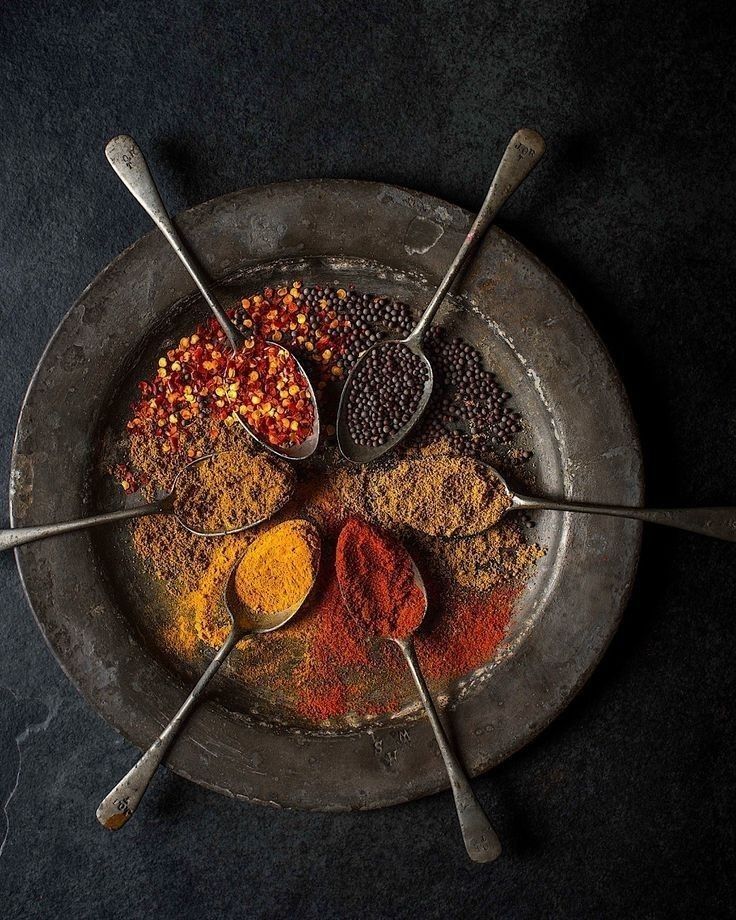 Close-up of Indian spices in metal spoons arranged on a rustic plate, showcasing chili flakes, mustard seeds, turmeric, cumin, and paprika used in Dhoom’s fine dining spice pairing.