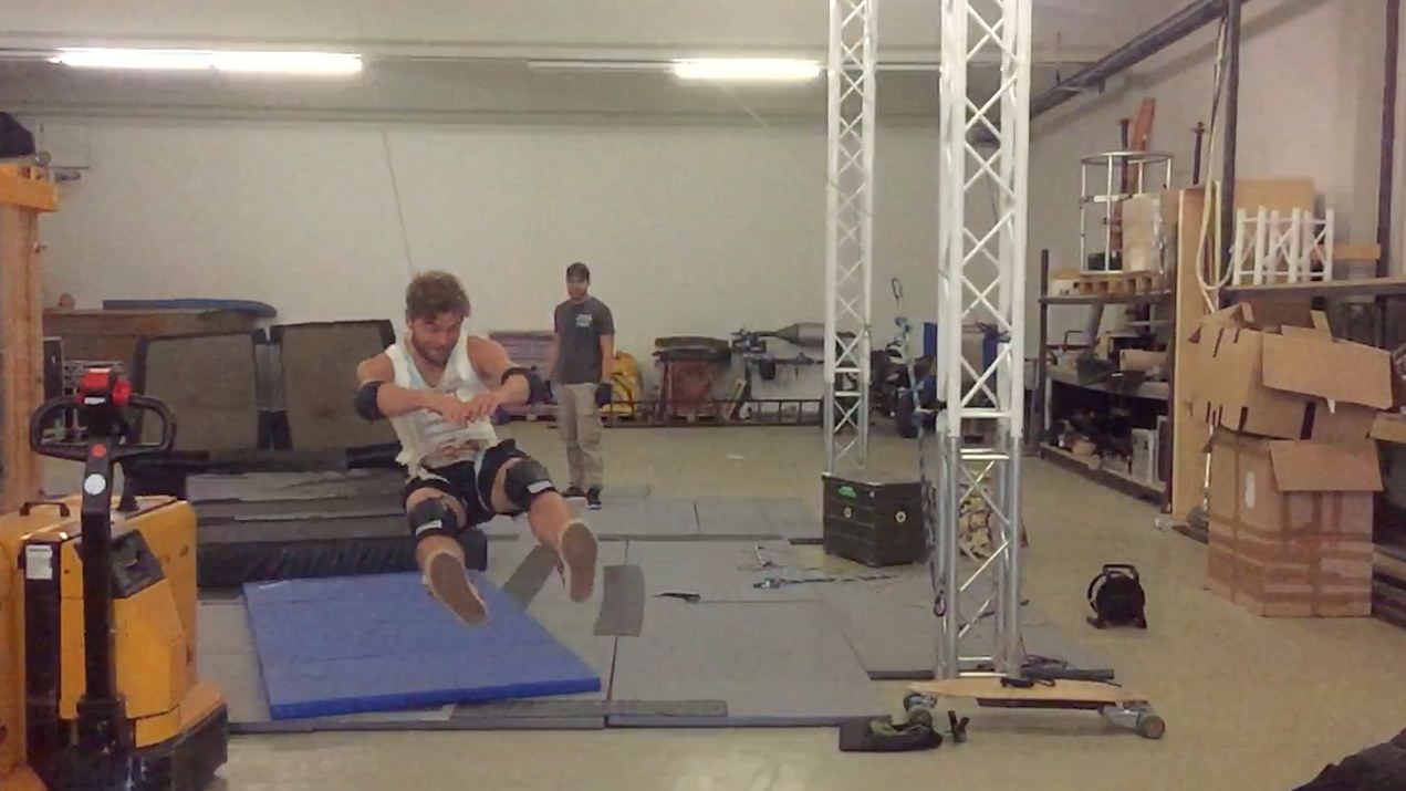 Training hall with truss, mats and a lifting rig: the rigger builds the setup while a colleague spots and watches from outside