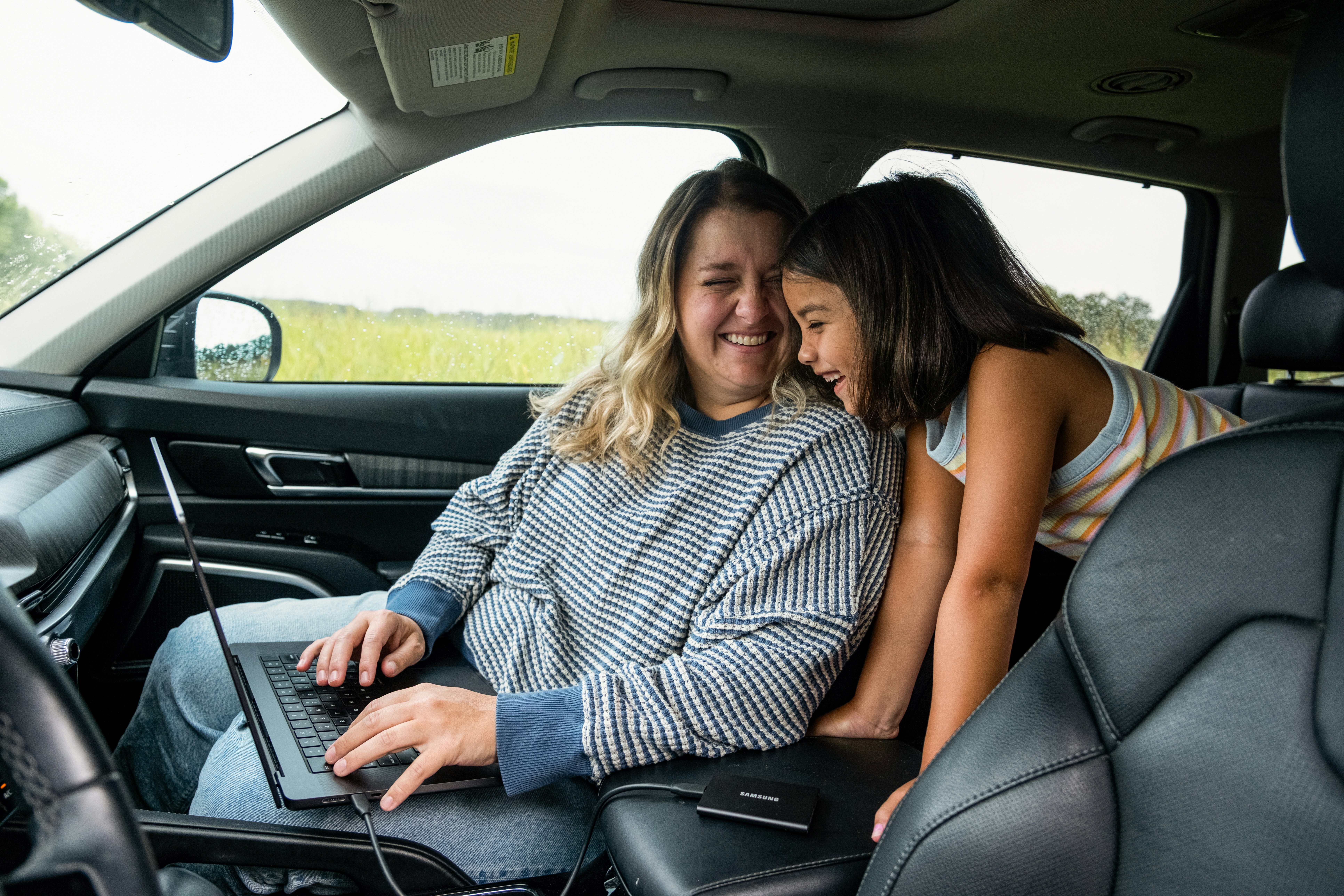 Woman works on laptop with child in car.
