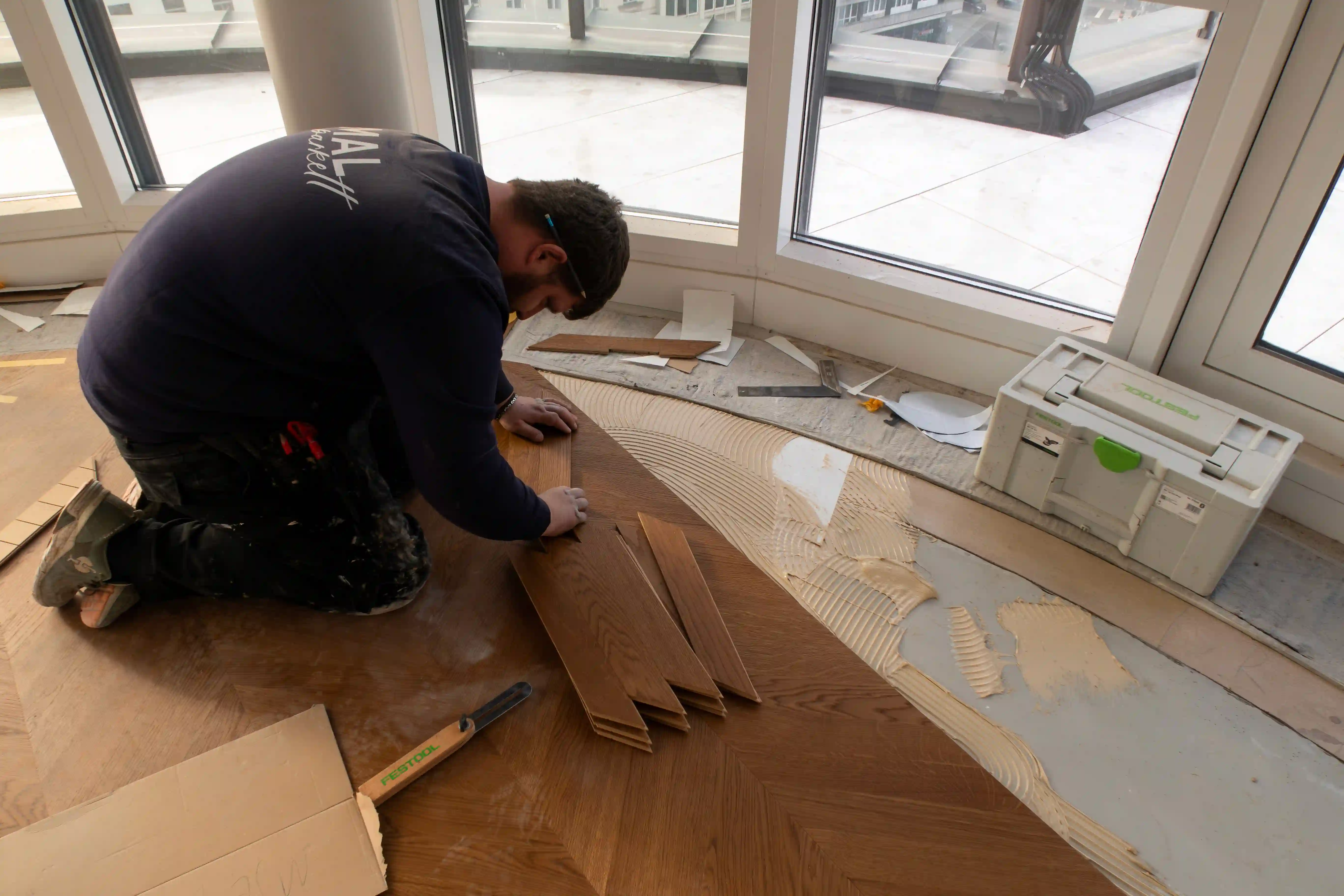 Bodenleger passt Chevron-Parkettelemente präzise an und verlegt sie sorgfältig im Innenraum.