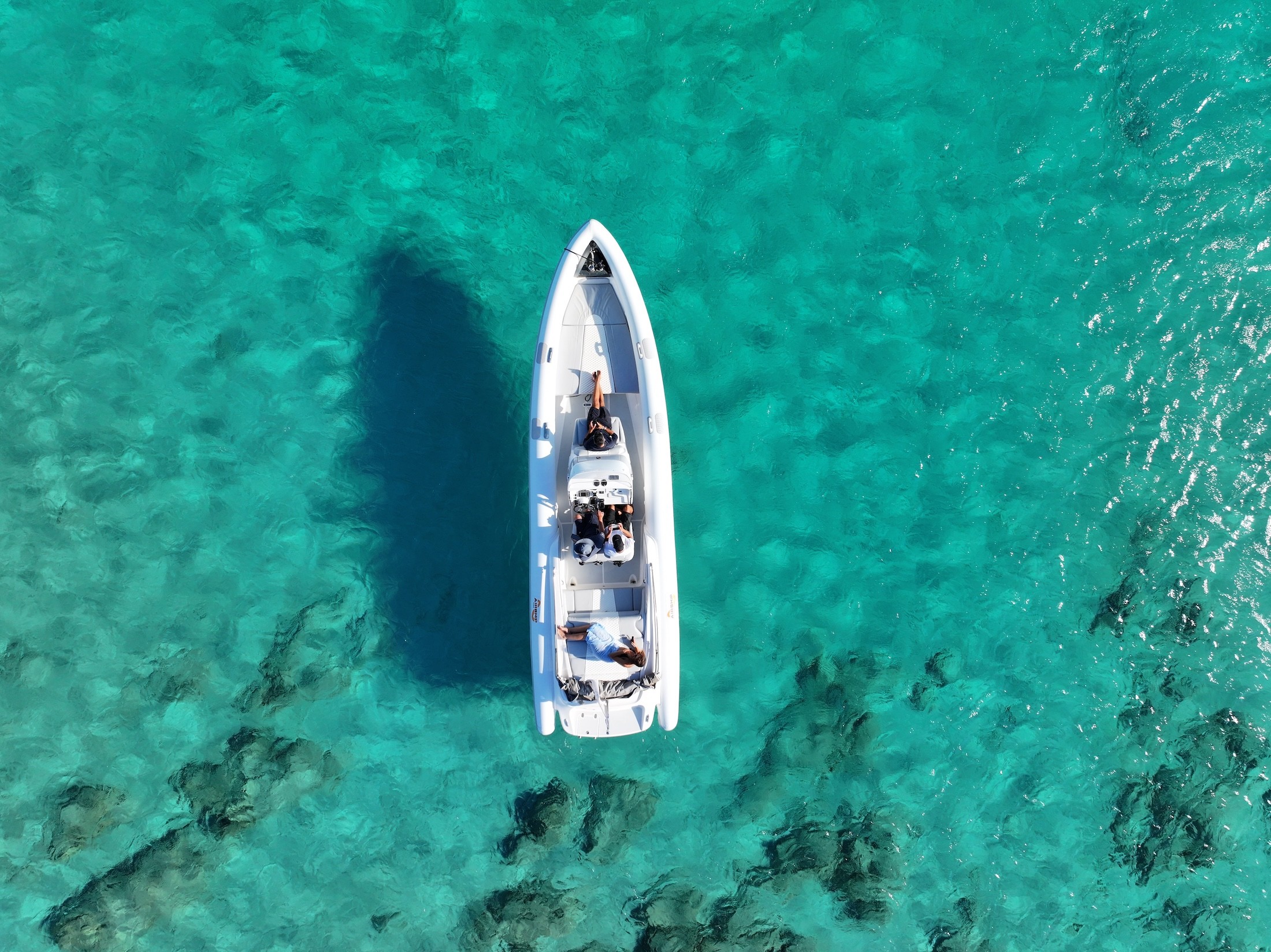 Aerial view of a white yacht anchored in a secluded turquoise lagoon surrounded by limestone cliffs and Mediterranean vegetation.