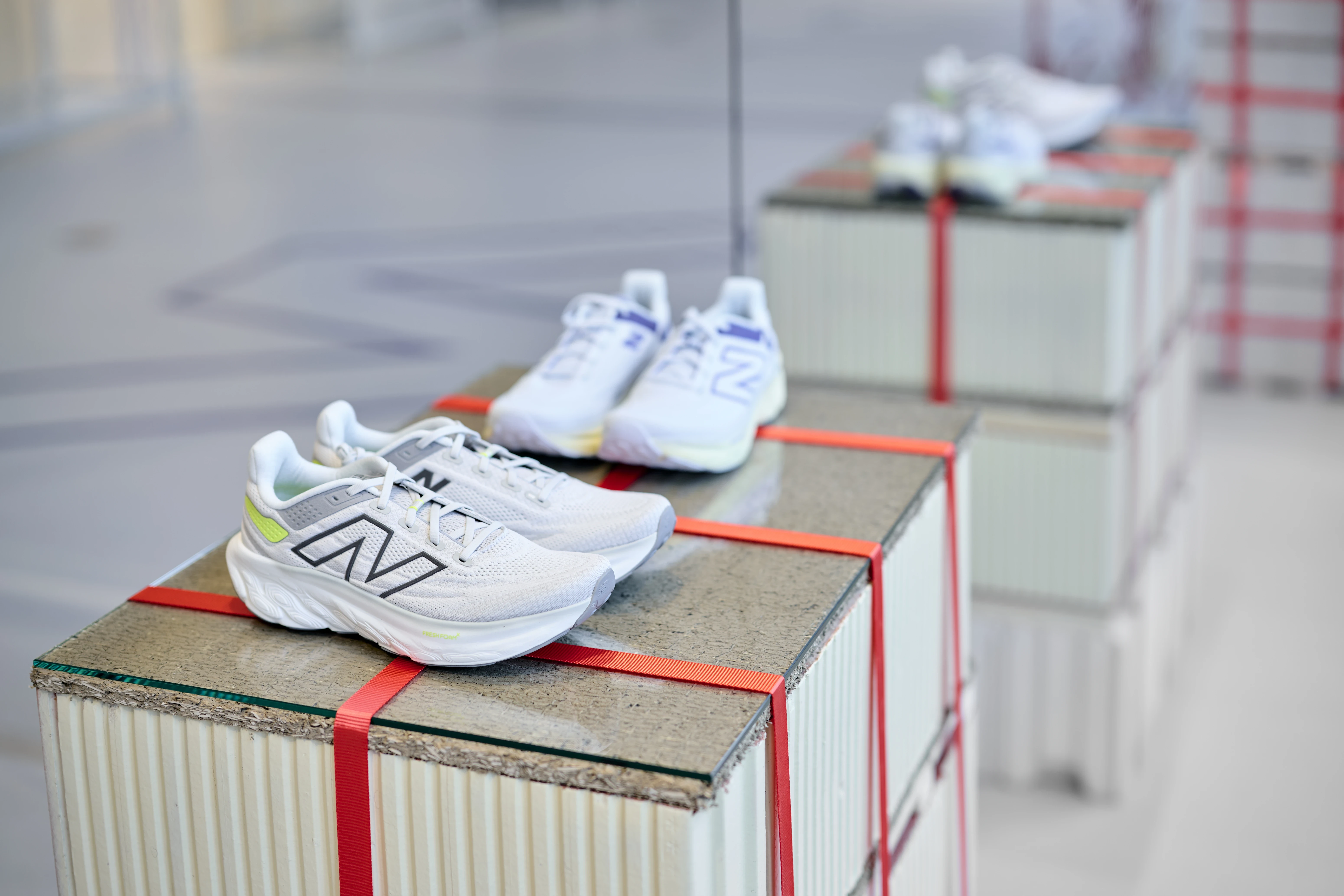 White New Balance sneakers on stone-topped crate plinths secured with red tension straps at the pop-up store.