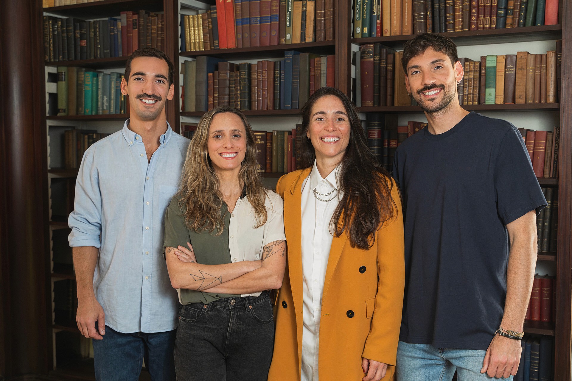 Cuatro integrantes del equipo posando sonrientes frente a una biblioteca.