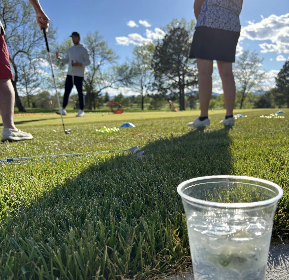 A group of students at the edge of a green, chipping balls towards net targets.