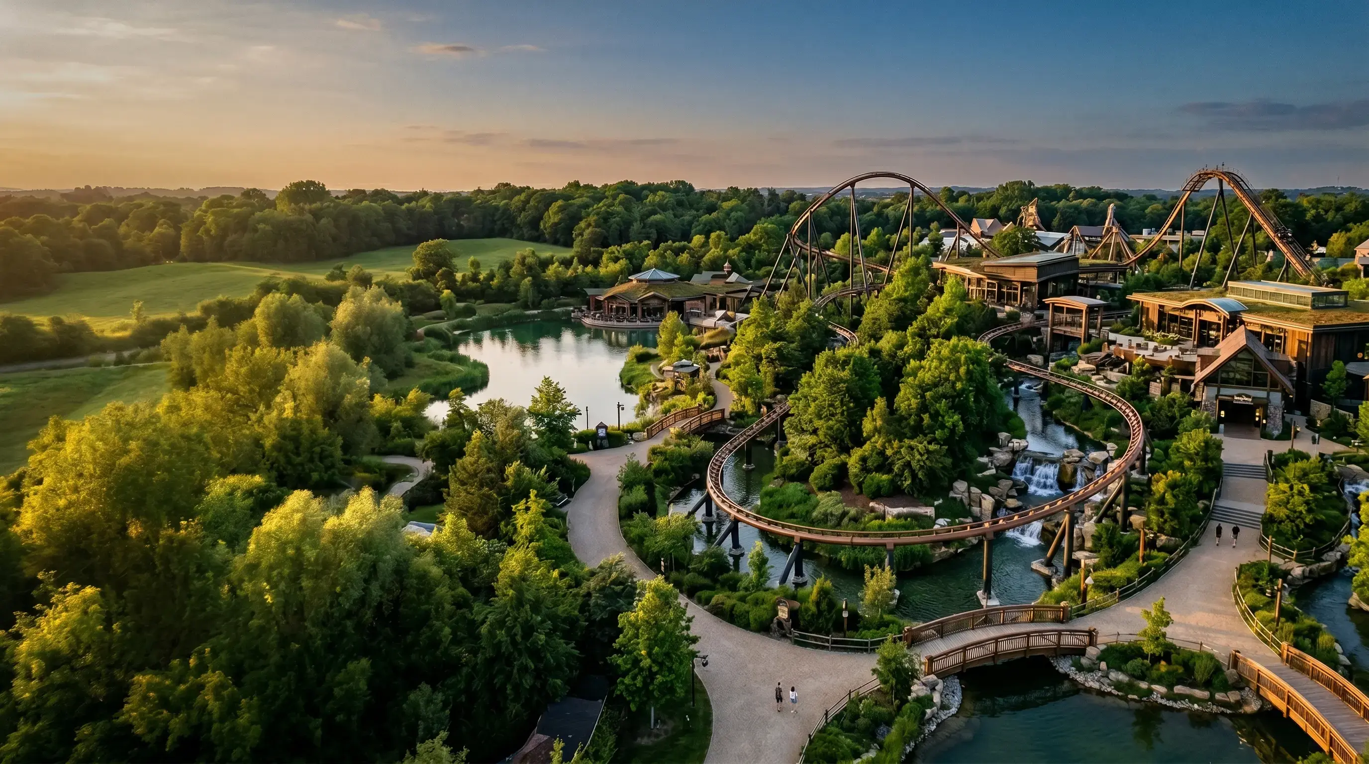 Aerial view of a wooded theme park at sunset with a lake and a roller coaster
