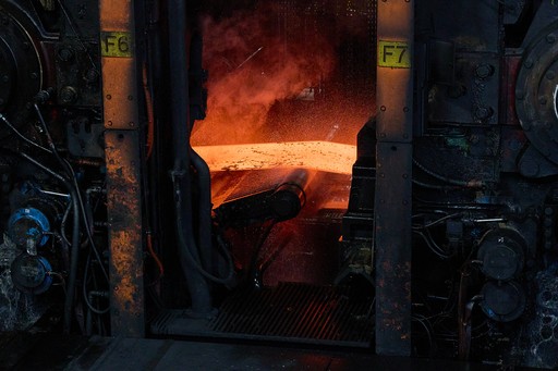 Gros plan sur une plaque d'acier en fusion rouge vif sortant d'un laminoir industriel, générant de la fumée et des projections d'eau.