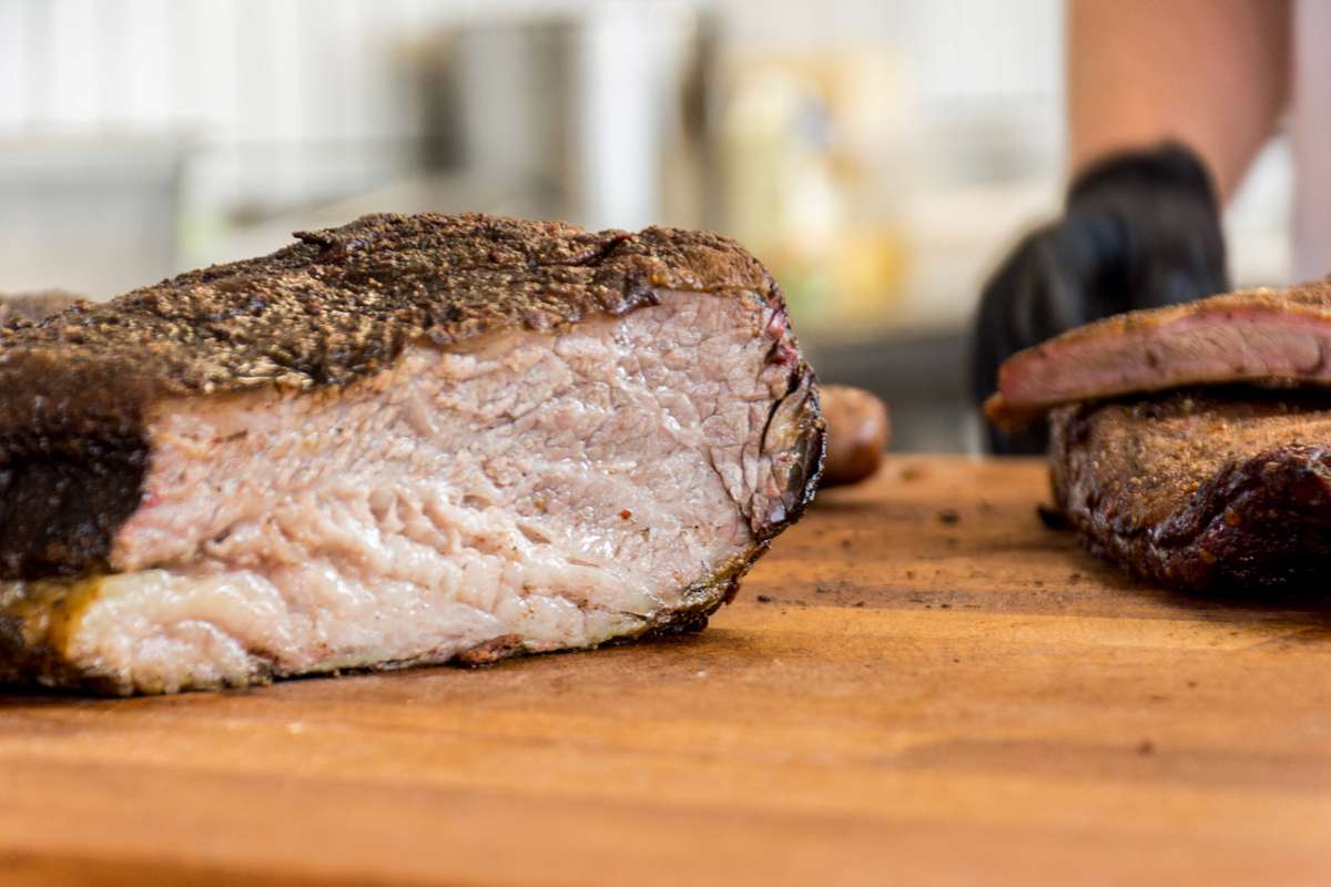A sliced piece of seared steak with a dark crust and pink center rests on a wooden cutting board.
