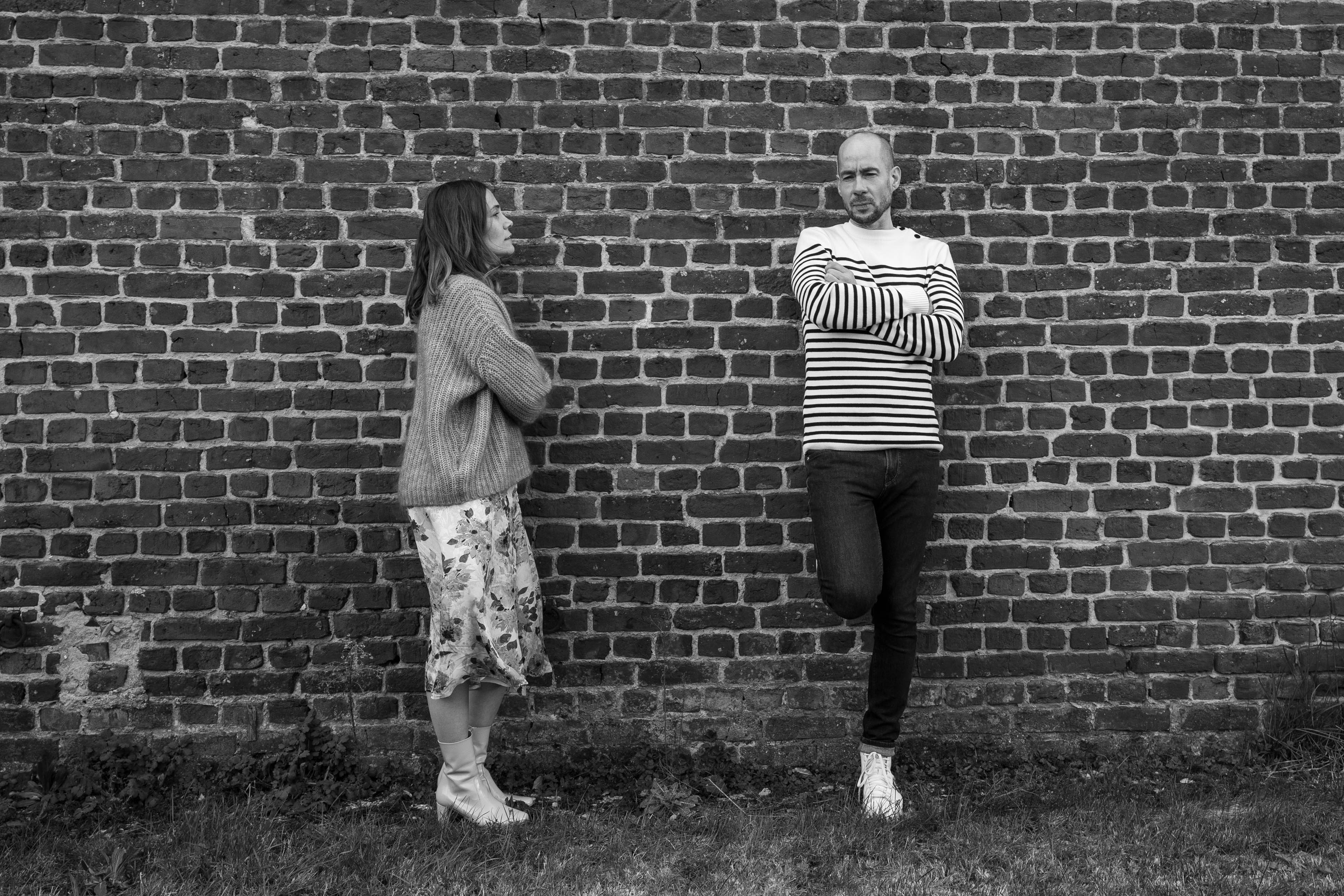 Close-up portrait of a person wearing a gray insulated hooded jacket with the hood up, showing their face framed by the hood against a light background.