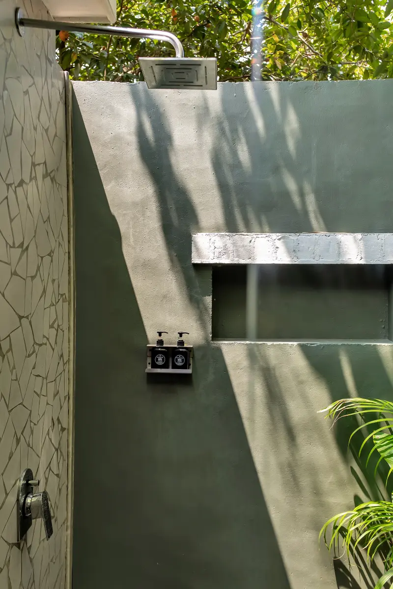 Premier Room private outdoor shower at Vedic Village Kodungallur with mosaic tile walls and dappled greenery in a secluded garden setting