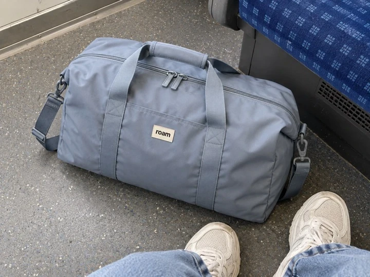 Illustrative buyer phone photo of a blue-grey weekender beside a train seat