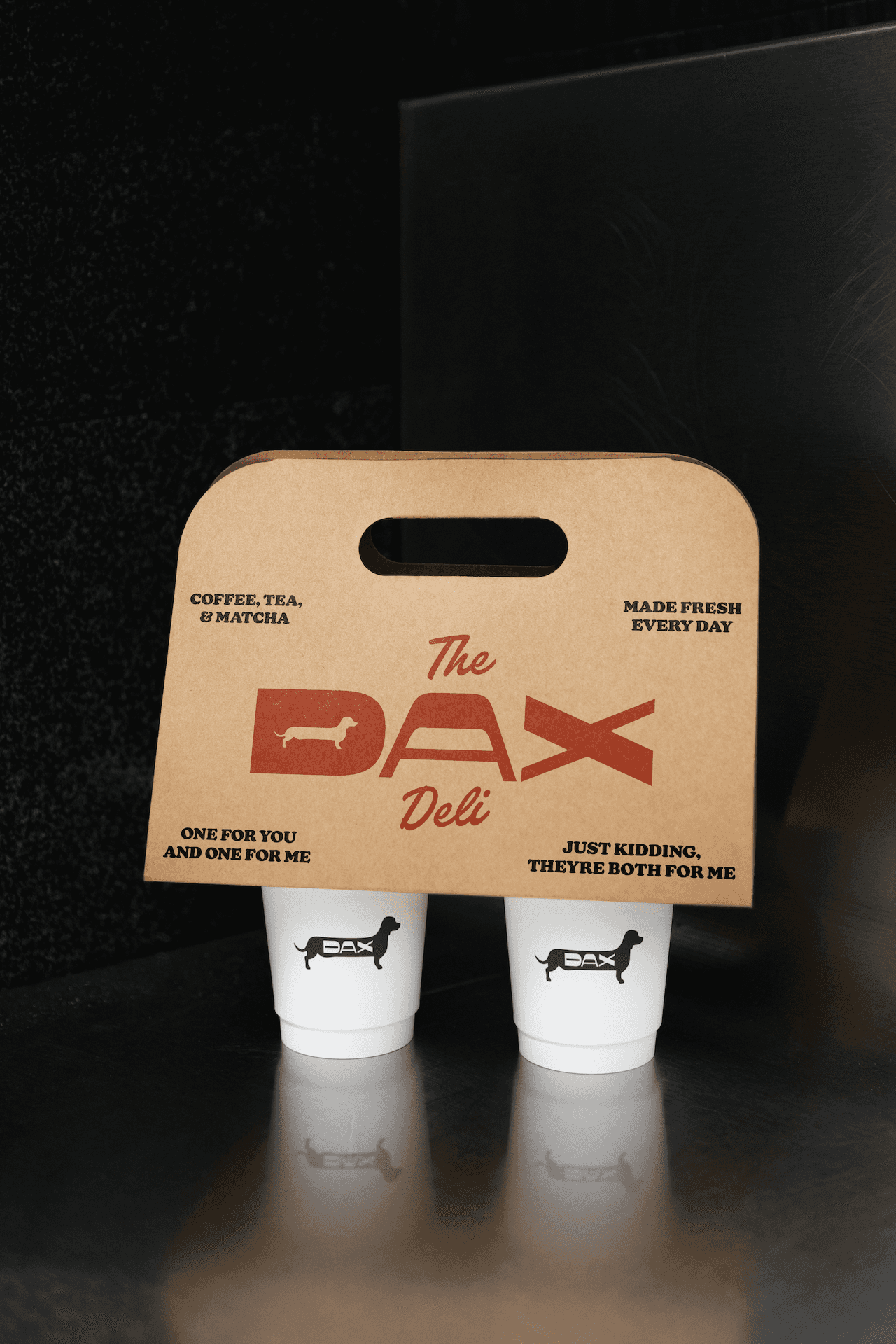 A coffee cup holder branded with The Dax Deli logo