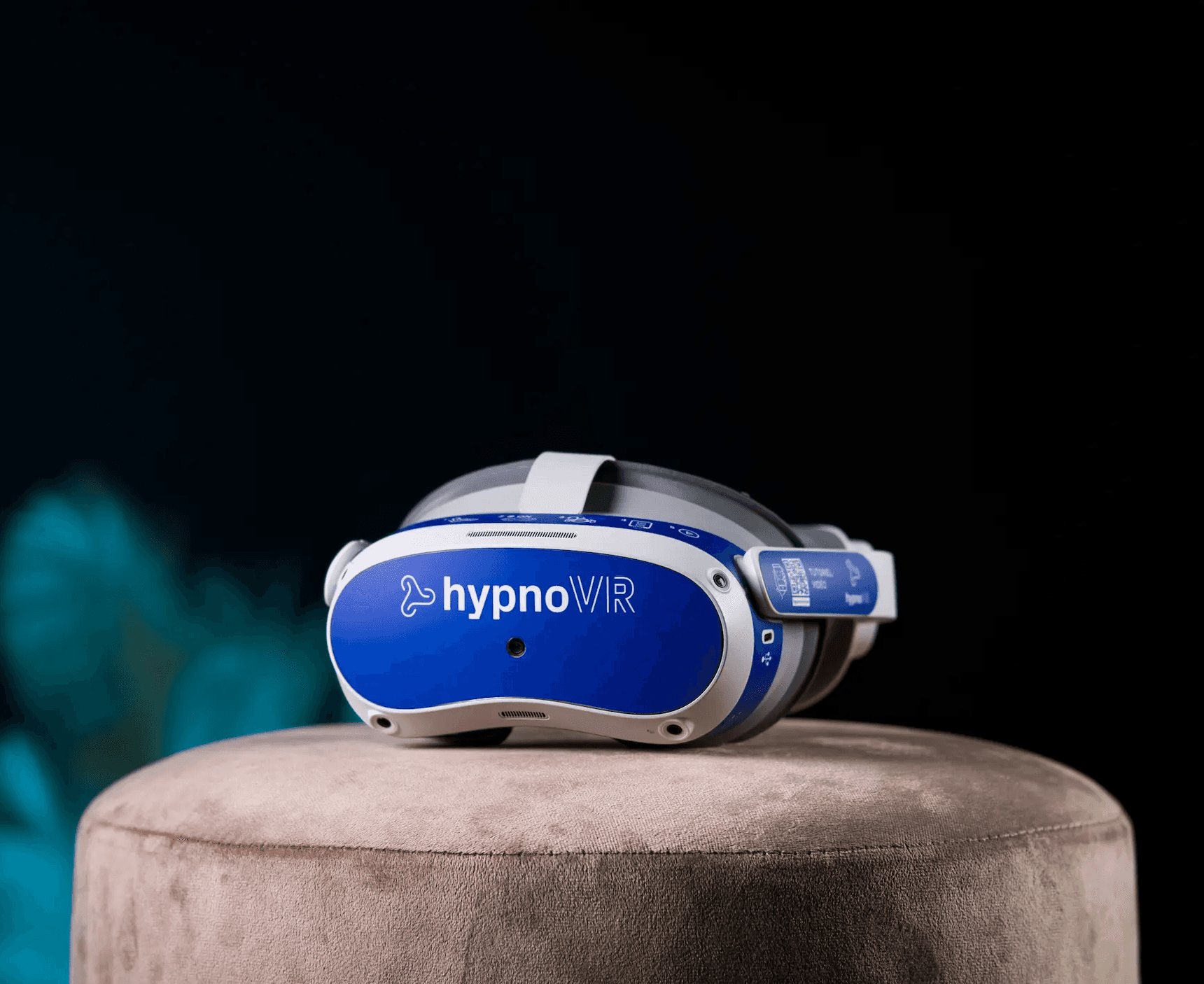 Casque de réalité virtuelle HypnoVR posé sur un support en velours beige, sur fond sombre avec un éclairage bleu en arrière-plan