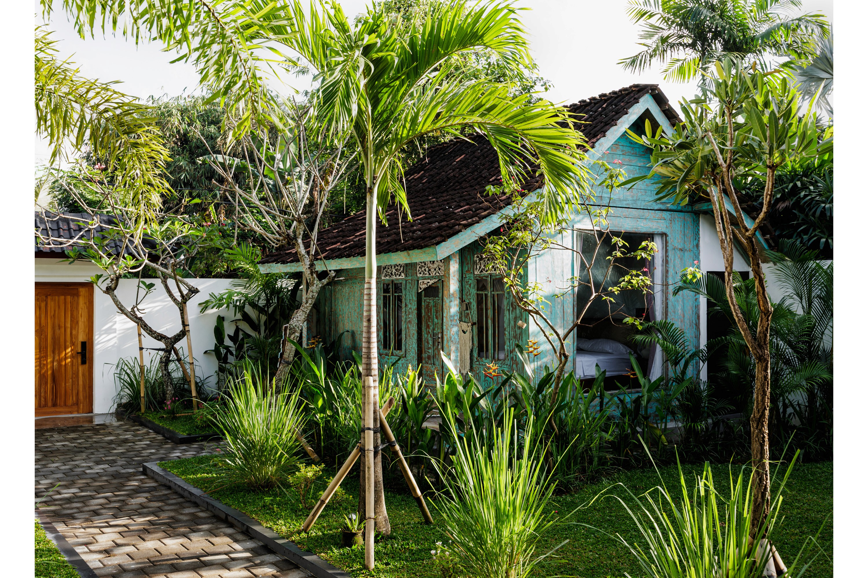 Traditional tropical villa with vintage wooden facade, lush garden, and palm trees.