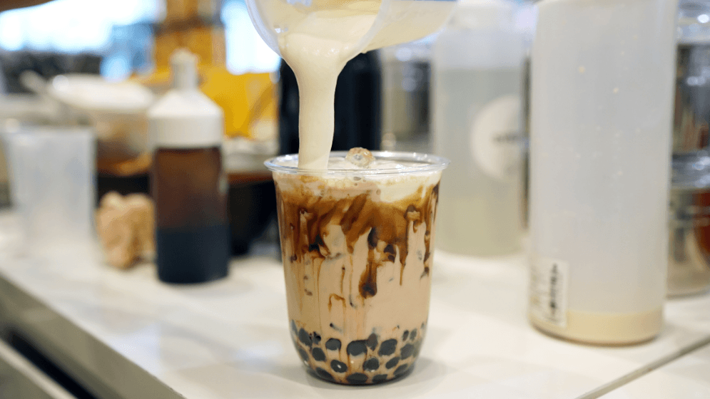 Pouring cream cheese into glass of milk tea with black sugar syrup and black pearl