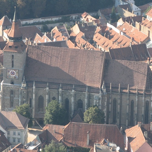 赤い瓦屋根に囲まれた、背の高い時計塔を持つ大きな歴史的教会を空中から見下ろす光景です。