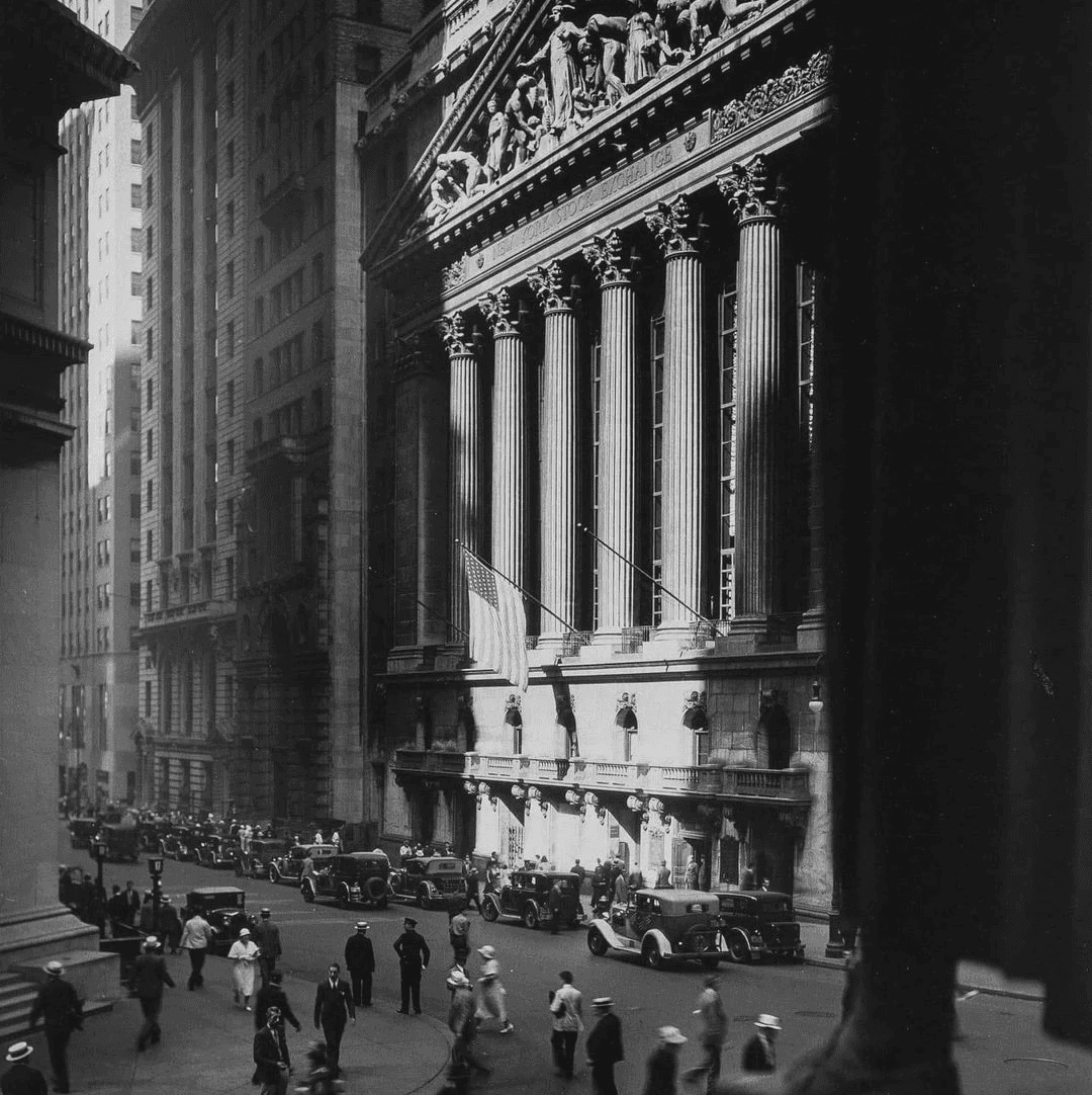 A young person with curly hair smiles at the camera while sitting in front of a laptop against a dark background.