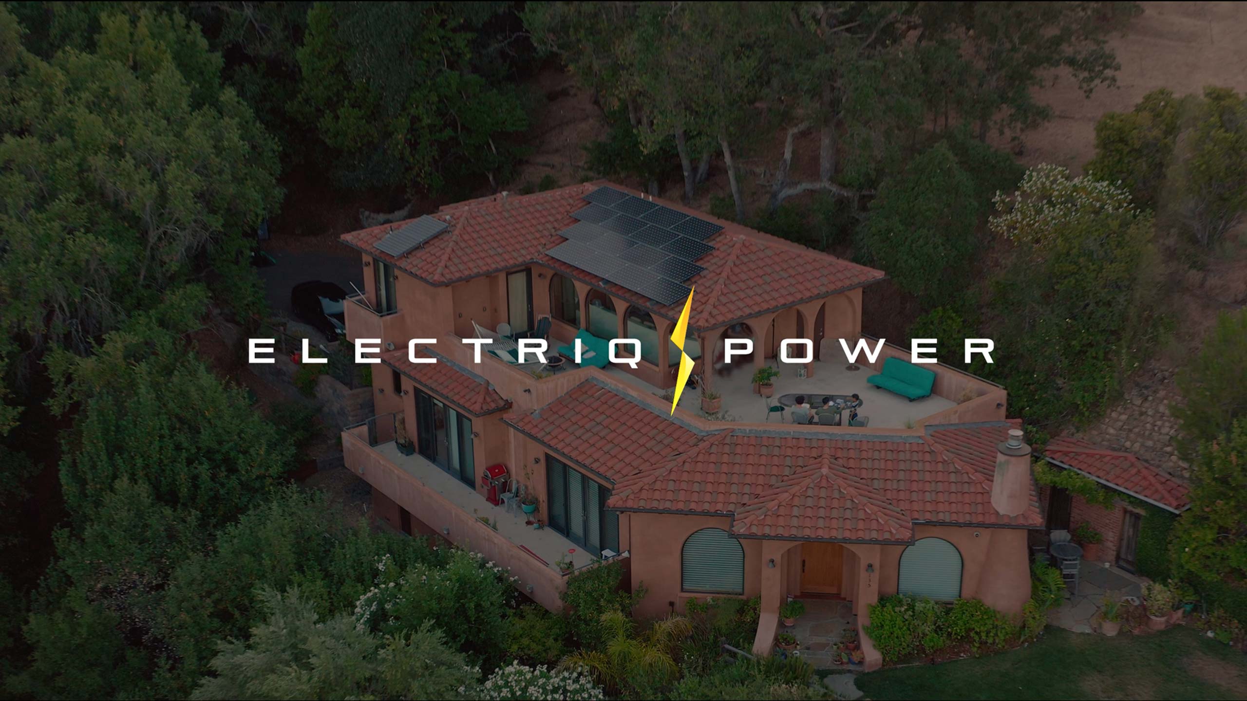 Video still showing the Electriq Power logo superimposed on a drone shot a house with solar panels