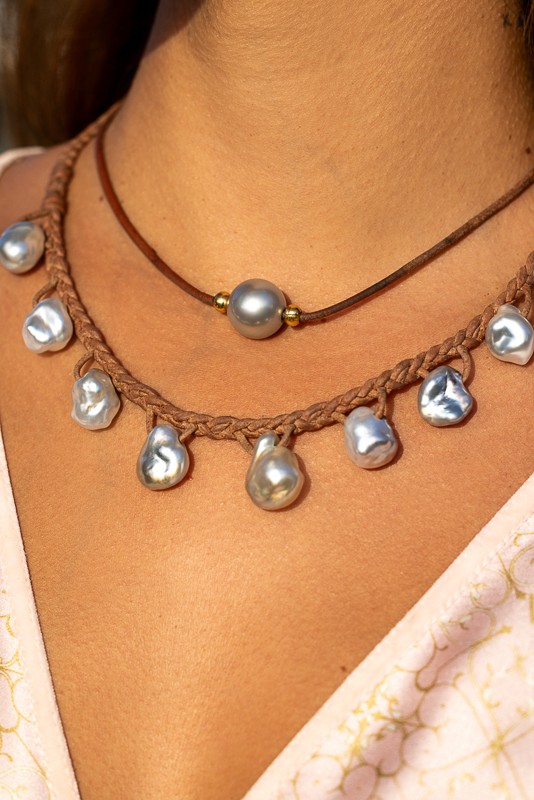 Close-up of a woman wearing Manos de Oro Saint Barth’s layered pearl necklaces—featuring baroque freshwater pearls and a central silver-toned pearl on braided leather, echoing coastal splendor and artisanal mastery.