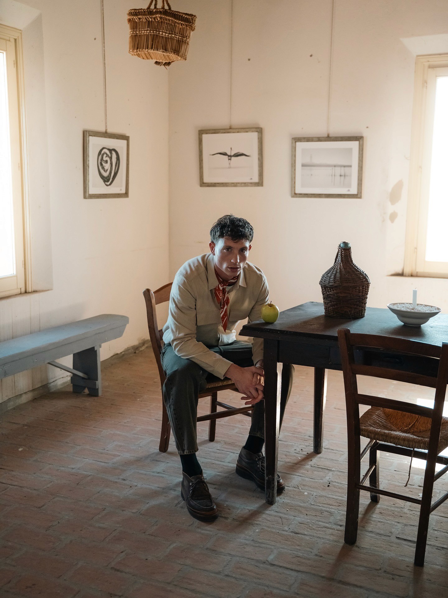 Mannequin assis dans une maison et portant maille, foulard imprimé et pantalon large de la marque Wooden Store, dans le lookbook FW25 de cette marque Italienne de pret-à-porter masculin