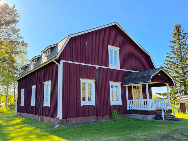 Ulkomaalattu tummanpunainen omakotitalo Lappajärvellä, valkoinen kuisti ja ikkunapuitteet, vihreä ja avara piha-alue