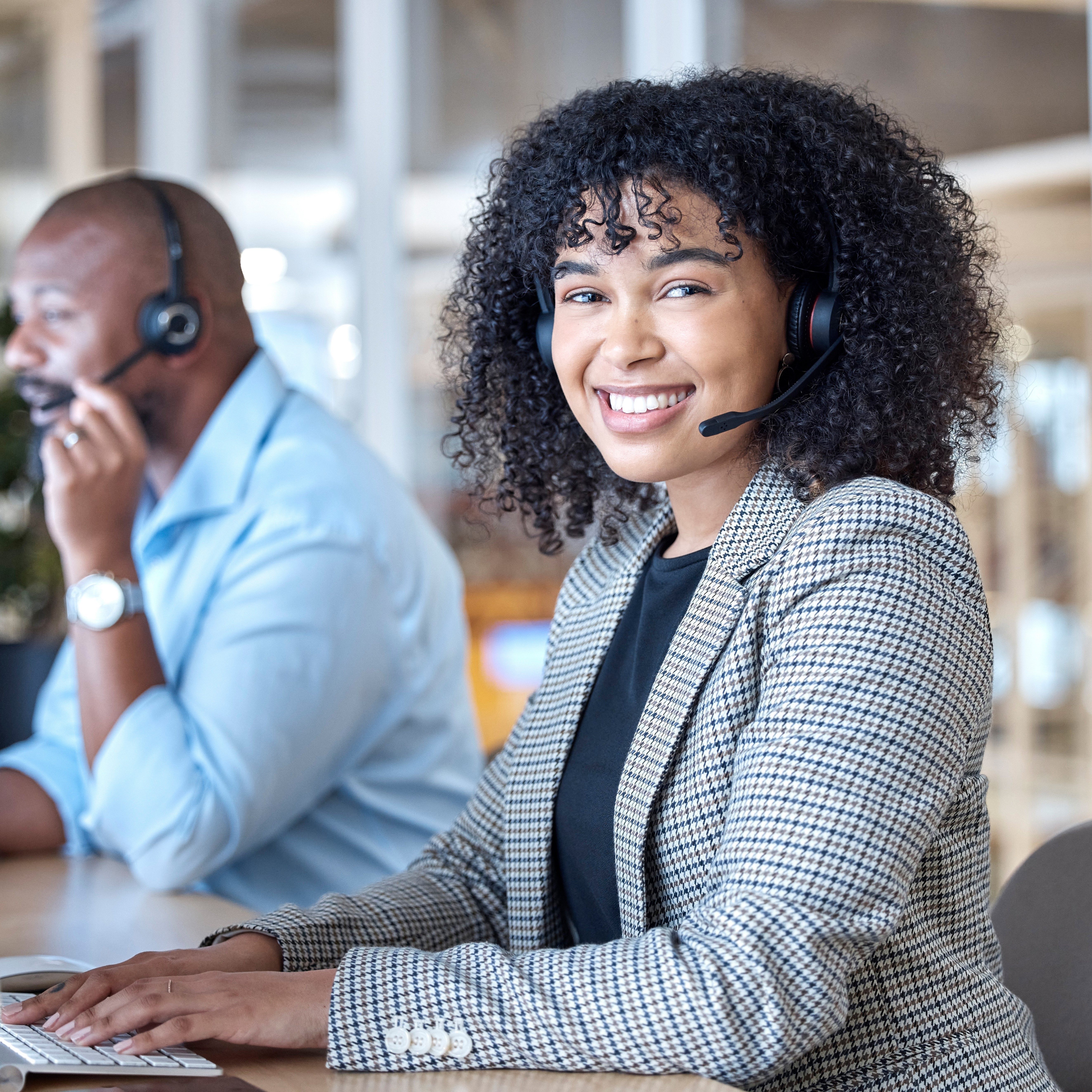 Cheerful customer service representative with headset working at a computer in a busy call center, providing professional assistance with a smile, exemplifying exceptional interpersonal talent and communication skills.