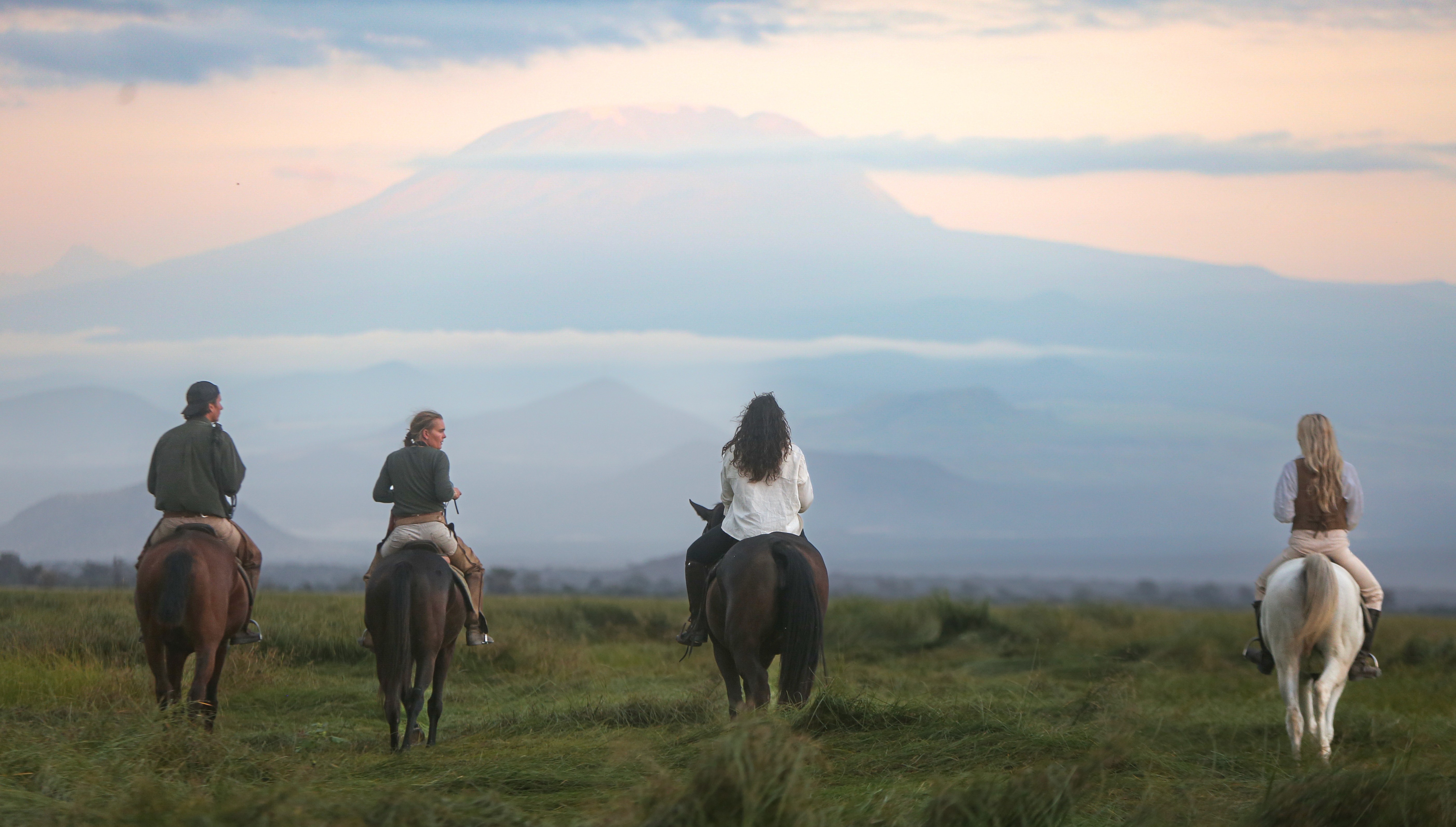 Kilimanjaro Elephant Ride, Arusha National Park, Tanzania – fyra ryttare till häst ses bakifrån rida mot ett högt berg i disigt morgonljus, ett vackert ögonblick på ridsemester i Afrika.