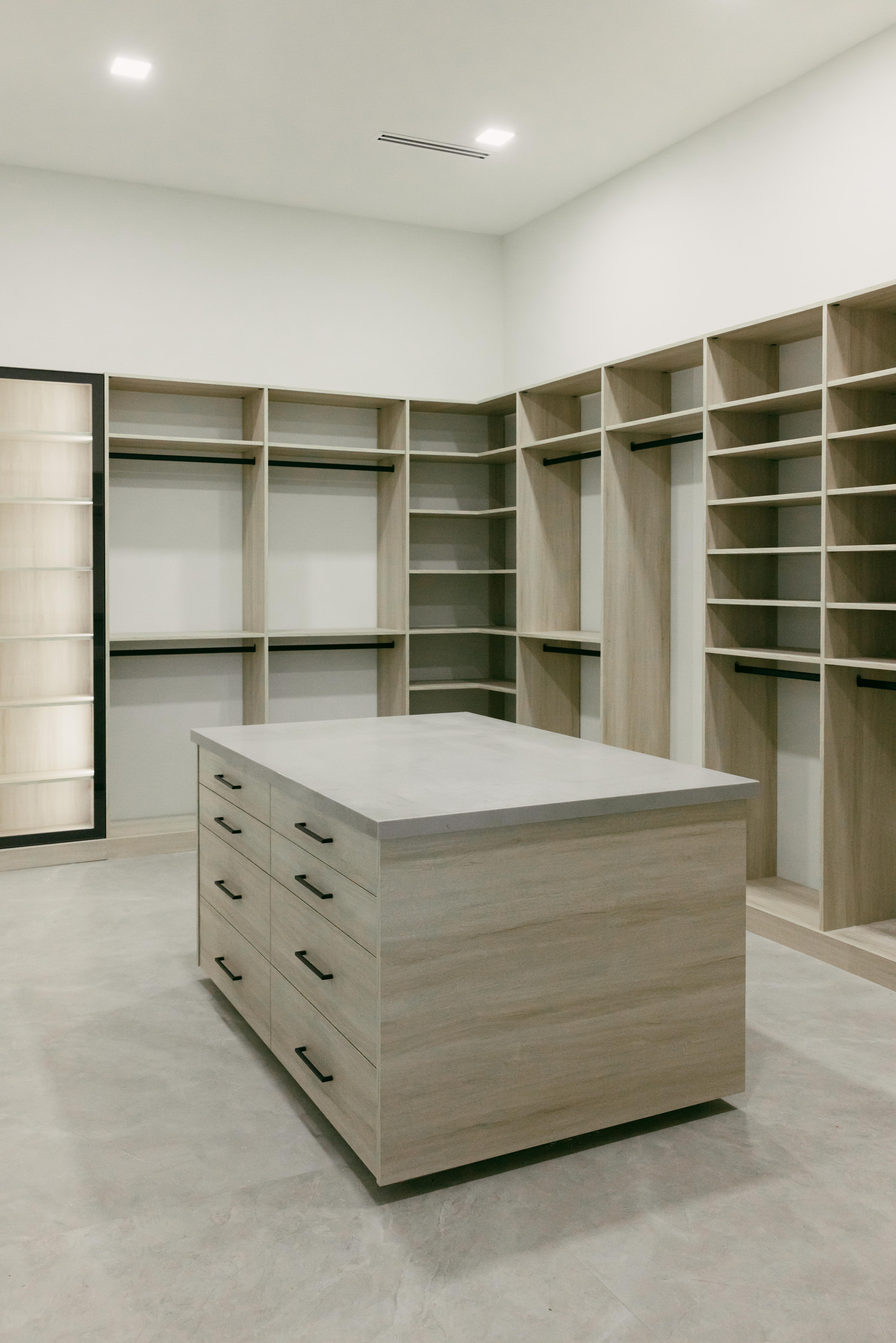 Modern walk-in closet with light wood shelving and a central island dresser.